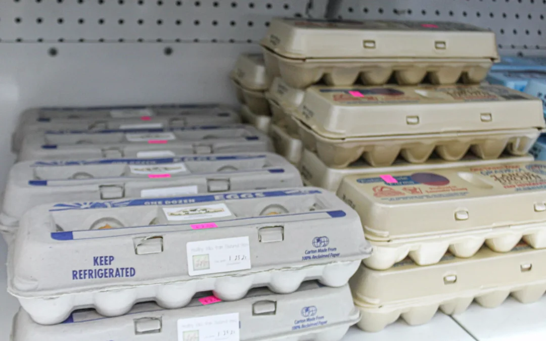 2.27.21-Leids-Market-Gallery-1-2-scaled-1 Several cartons of eggs are stacked on a grocery store shelf, each labeled with small pink price stickers.