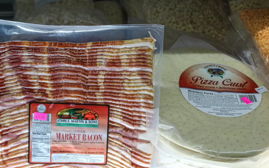 2.27.21-Leids-Market-Gallery-1-6-scaled-1 Packaged sliced bacon and packaged pizza crusts are displayed side by side on a grocery store shelf under bright lighting.