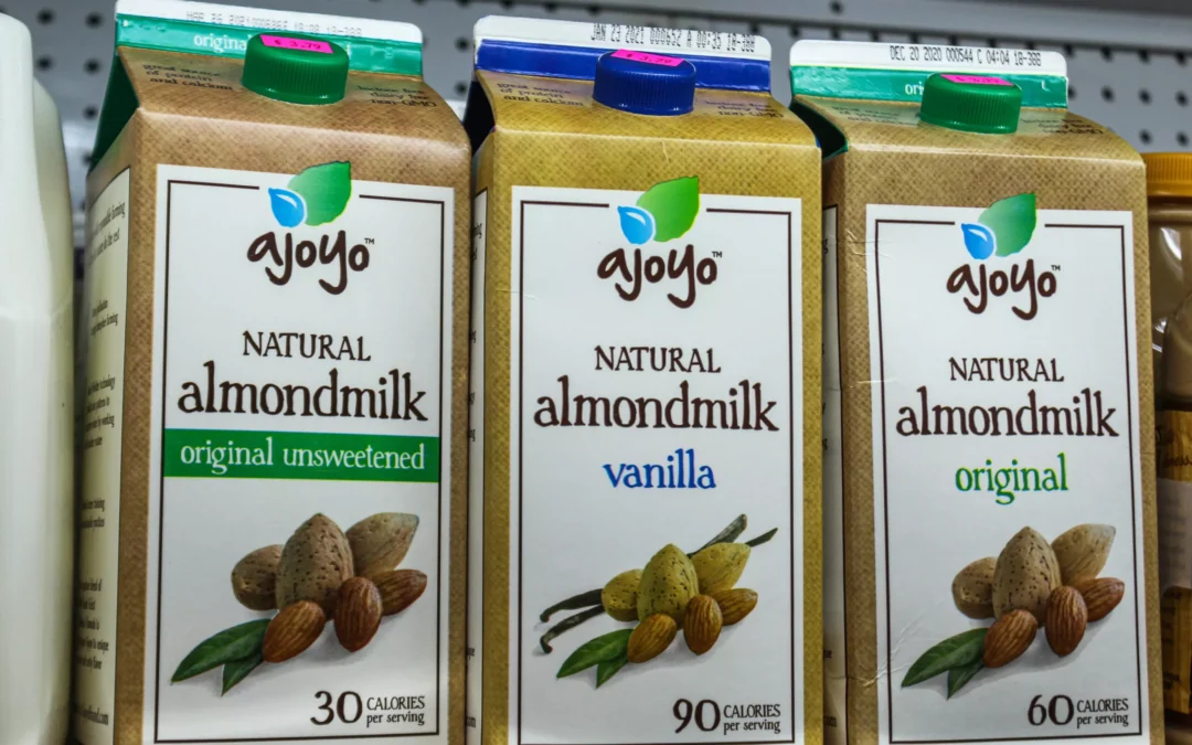 2.27.21-Leids-Market-Gallery-1-7-scaled-1 Three cartons of Ajoyo natural almondmilk—original unsweetened, vanilla, and original—are displayed on a store shelf. Each carton shows calorie content per serving.