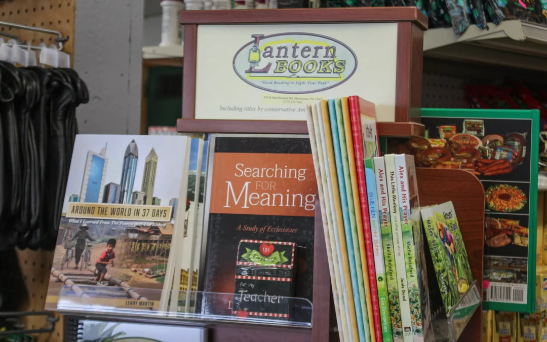 2.27.21-Leids-Market-Gallery-1-9-scaled-1 A wooden book display at Lantern Books holds various titles, including “Around the World in 37 Days” and “Searching for Meaning,” in a store setting.