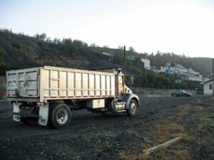 A dump truck full of coal driving down a gravel road.