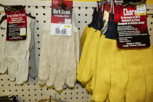 A pair of Boss brand work gloves hanging on a pegboard in a hardware store
