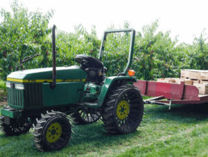 A green tractor pulling a trailer in an orchard