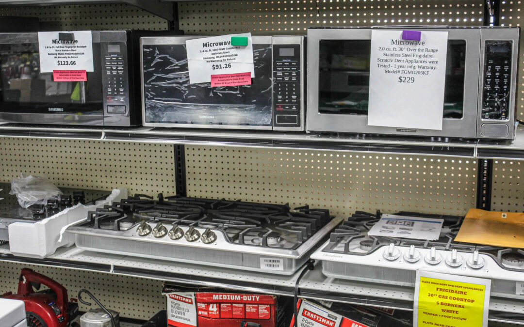Slate Road Supply Ephrata PA Shelf displaying various kitchen appliances including microwaves and a gas stove, each with price tags, in a store.