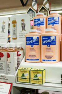 Store shelf displaying multiple bottles of Bismoline Medicated Powder, bottles of fire cider tonic, and boxes of Naked Bee Oatmeal & Honey soap.