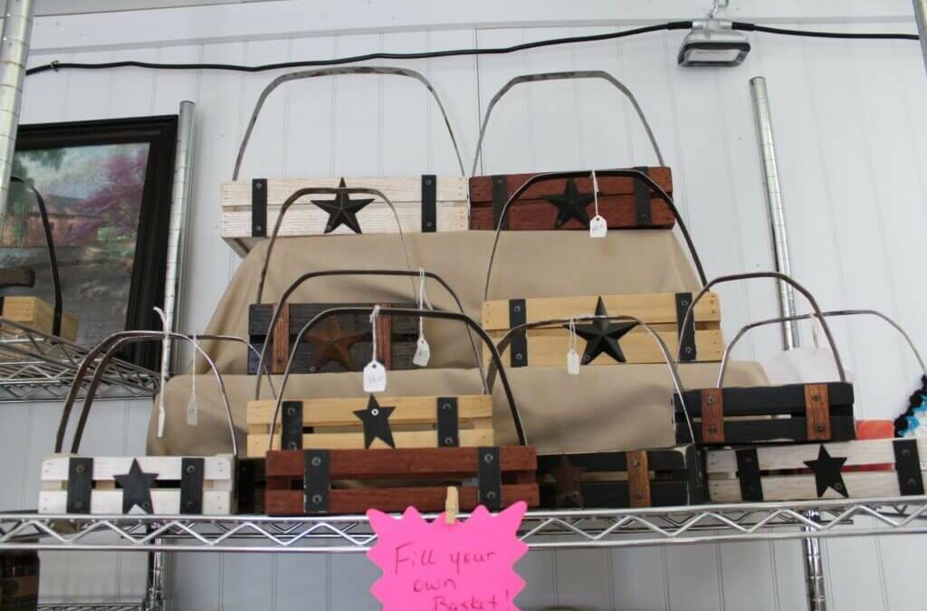Homegrown Cannery Stand New Holland PA A display of wooden baskets with star designs, arranged on metal shelves. Each basket has a price tag, and a pink sign below reads "Fill your own basket.