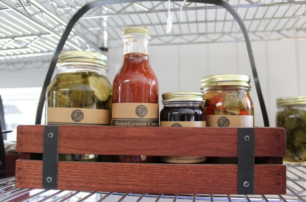 Homegrown Cannery Stand New Holland PA A wooden crate on a metal shelf holds a variety of glass jars filled with pickled vegetables, sauce, and jam.
