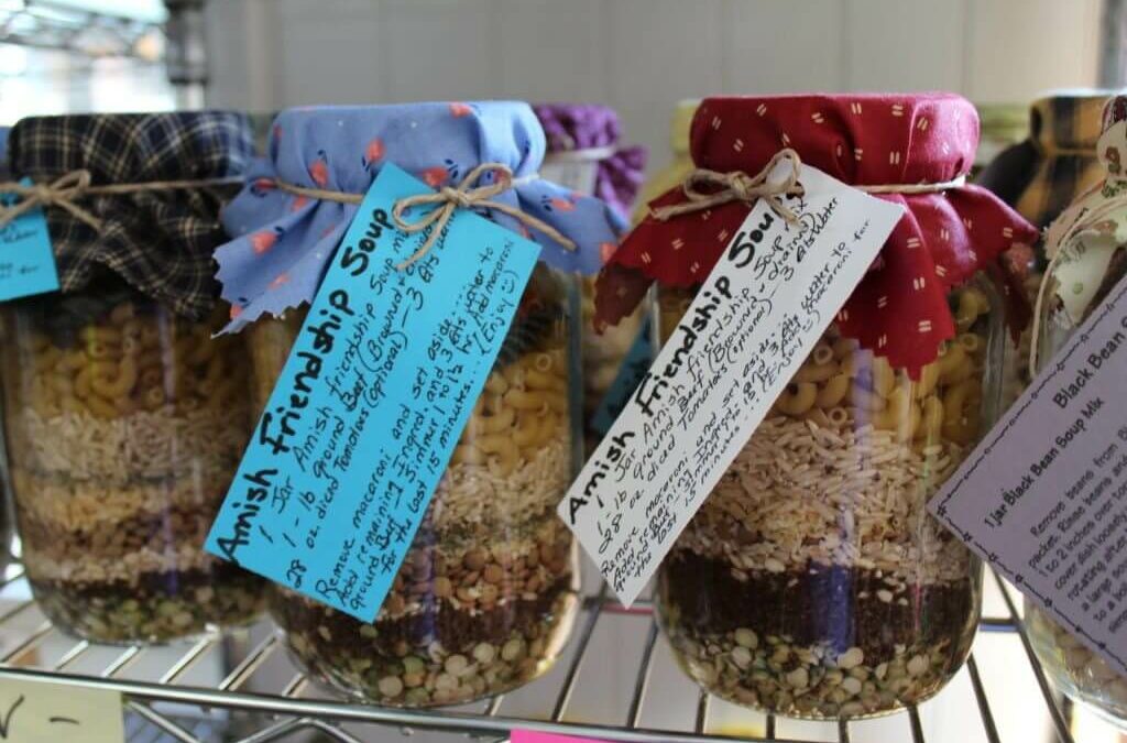 Homegrown Cannery Stand New Holland PA Jars of Amish Friendship Soup with layers of dry ingredients, covered with patterned cloths, labeled with handwritten tags, and displayed on a shelf.