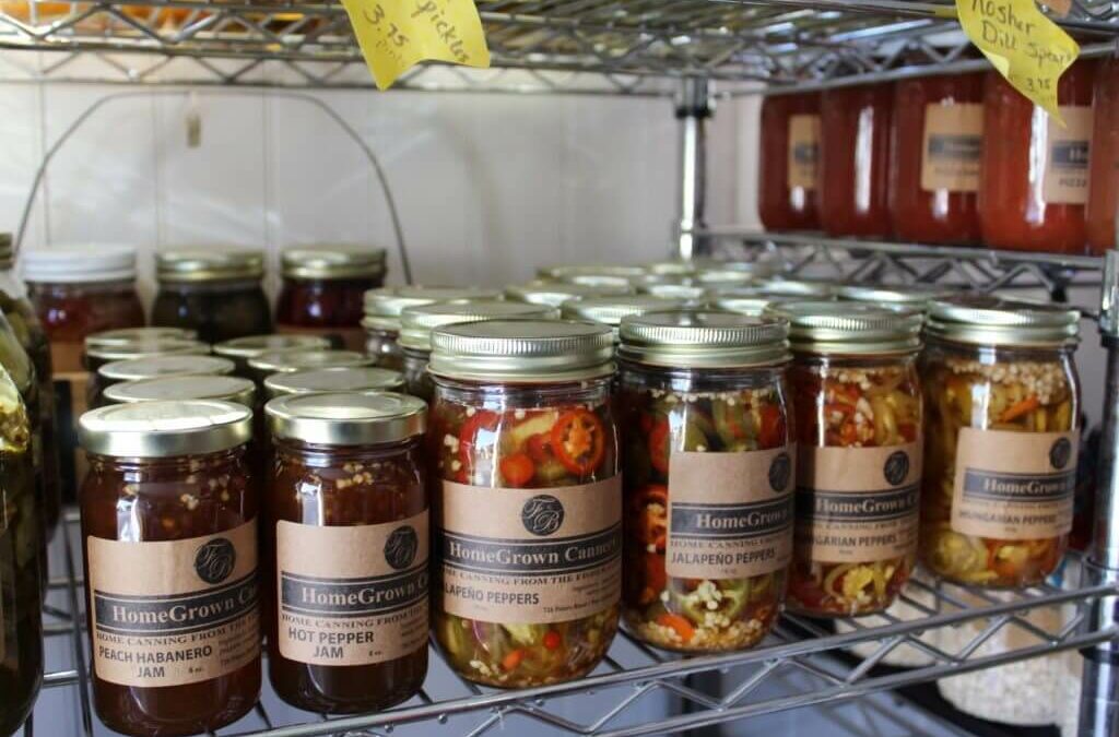 Homegrown Cannery Stand New Holland PA Shelves stocked with jars of HomeGrown canned goods, including peach habanero jam and jalapeno peppers. Some jars are stacked in rows, and there is a handwritten price label on the top shelf.