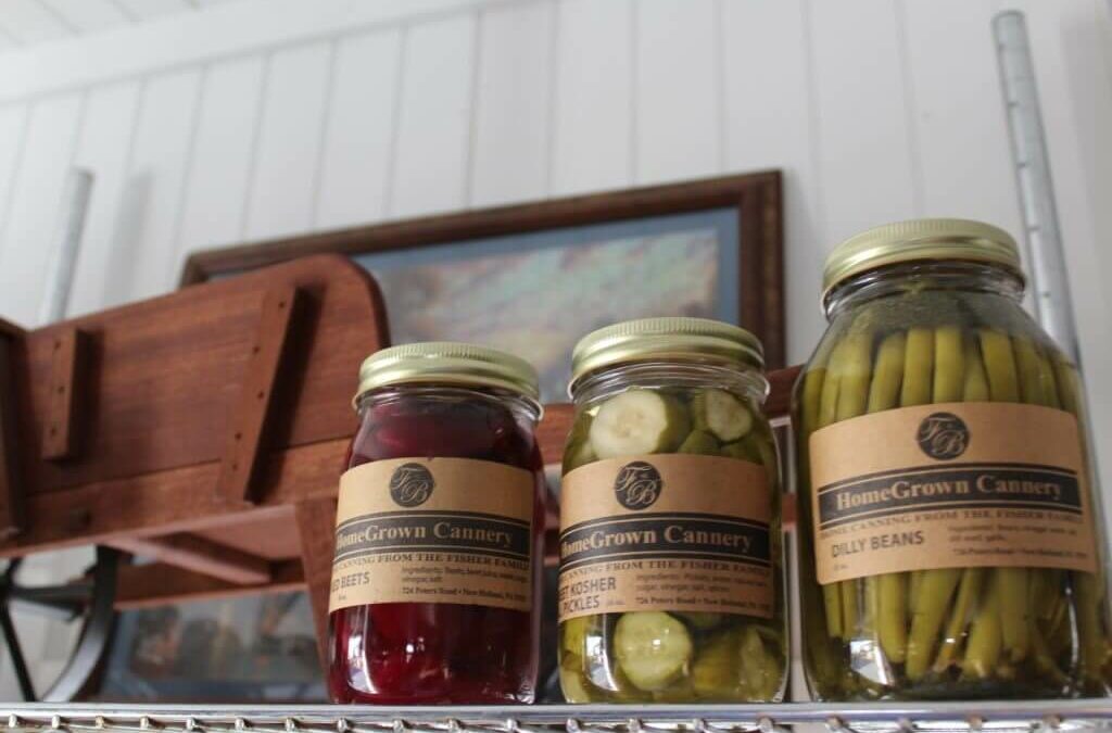 Homegrown Cannery Stand New Holland PA Three jars of preserved vegetables labeled "HomeGrown Cannery" are displayed on a shelf; the jars contain beets, kosher pickles, and dilly beans.