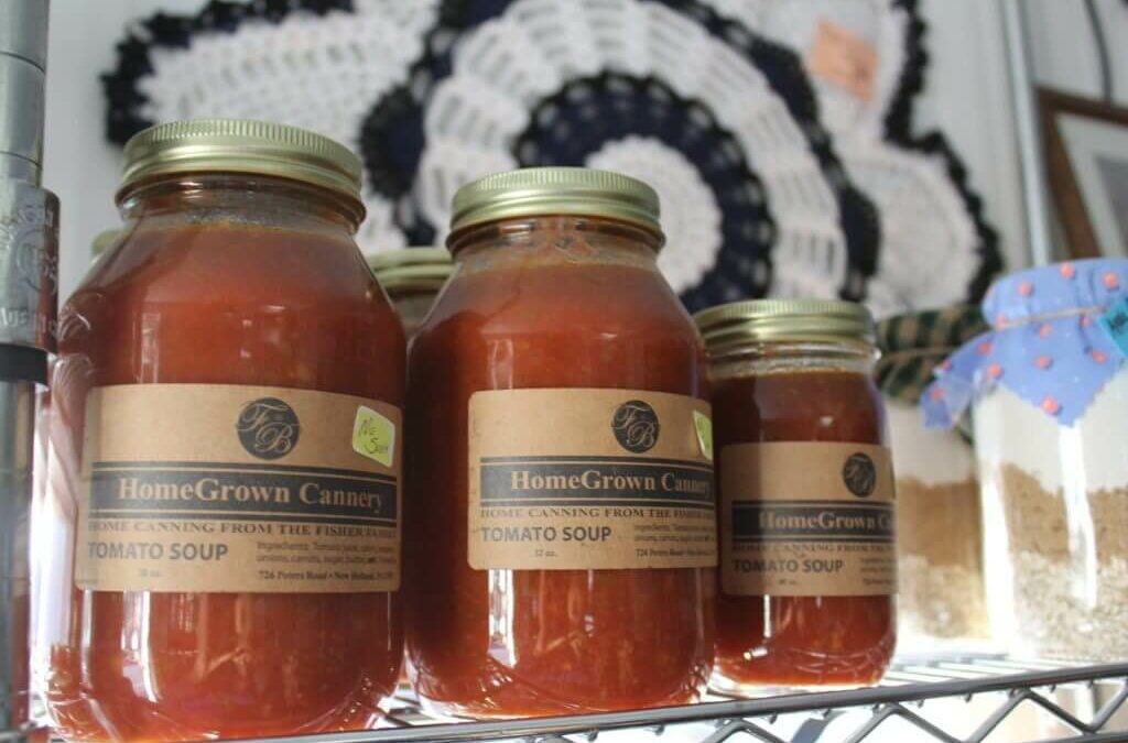 Homegrown Cannery Stand New Holland PA Jars of homemade tomato soup from HomeGrown Cannery are displayed on a shelf, alongside other canned goods and a crocheted decorative item on the wall behind them.