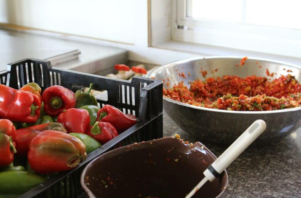 Homegrown Cannery Stand New Holland PA A kitchen counter with a crate of red and green bell peppers, a metal bowl filled with chopped peppers, and a brown bowl with a spatula.