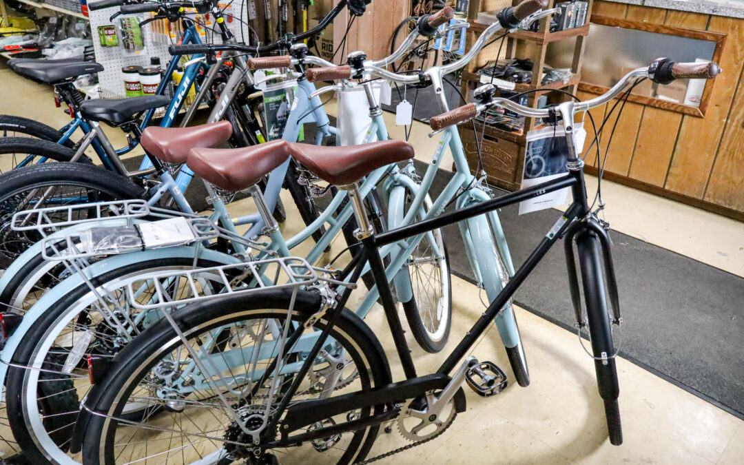 Weaver's Bike Shop Ephrata PA A row of bicycles, including black and light blue models with handlebars and baskets, are displayed indoors in a store with wooden walls and shelves of various items in the background.