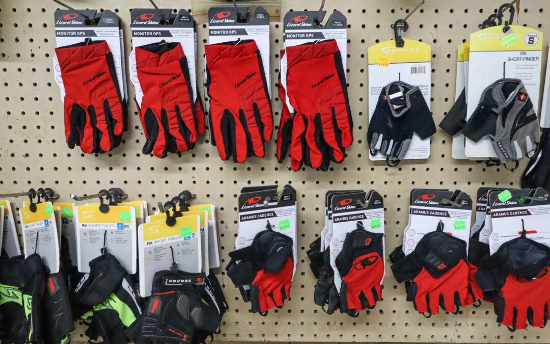 Weaver's Bike Shop Ephrata PA A display of various red and black biking gloves hanging on hooks in a store, neatly arranged on a perforated board. Some pairs are still in packaging with tags visible.