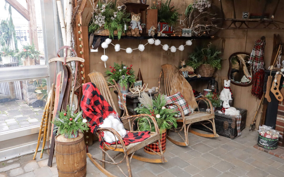 Reiff's Farm Market Ephrata PA Rustic winter-themed scene with wooden rocking chairs, plaid blankets, greenery, and vintage decor, including snowshoes and sleds, in a cozy, enclosed patio setting.