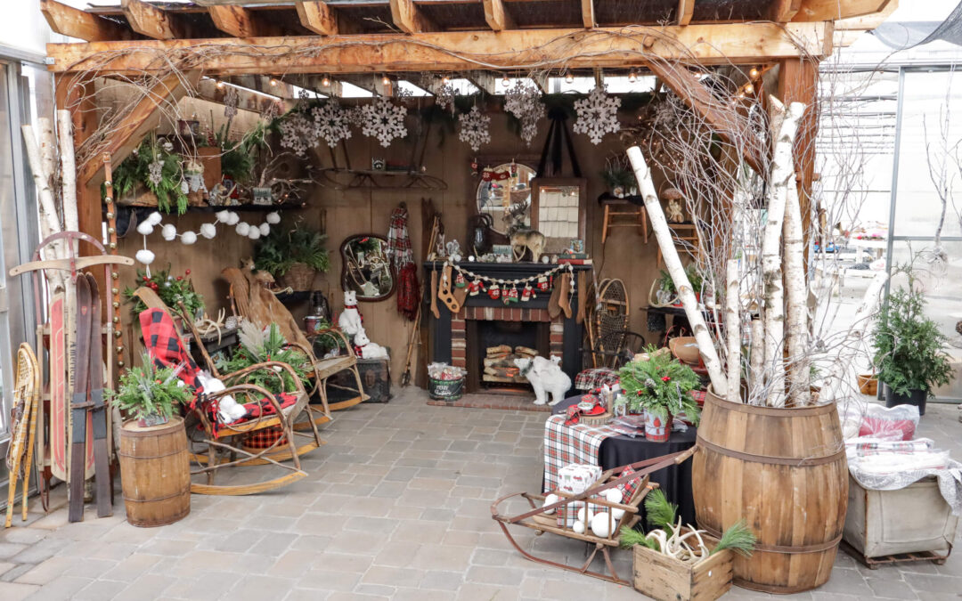 Reiff's Farm Market Ephrata PA Rustic Christmas-themed display with wooden chairs, a faux fireplace, skis, and holiday decorations under a pergola. Snowflakes and string lights hang from the wooden beams.