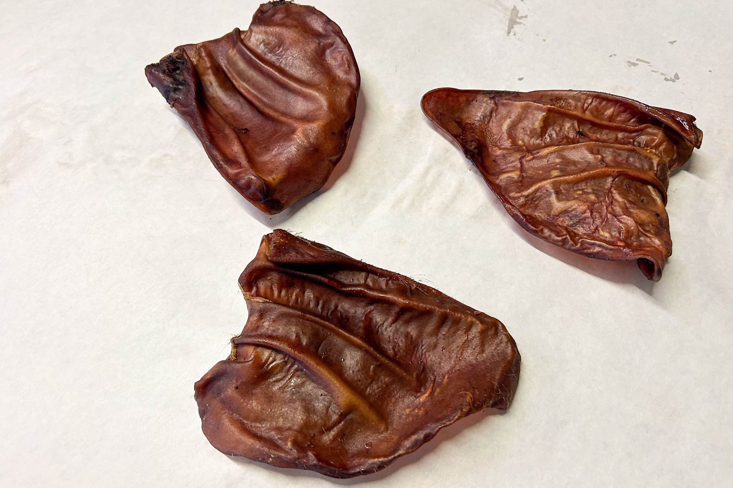 Three dried pig ears placed on a white surface.