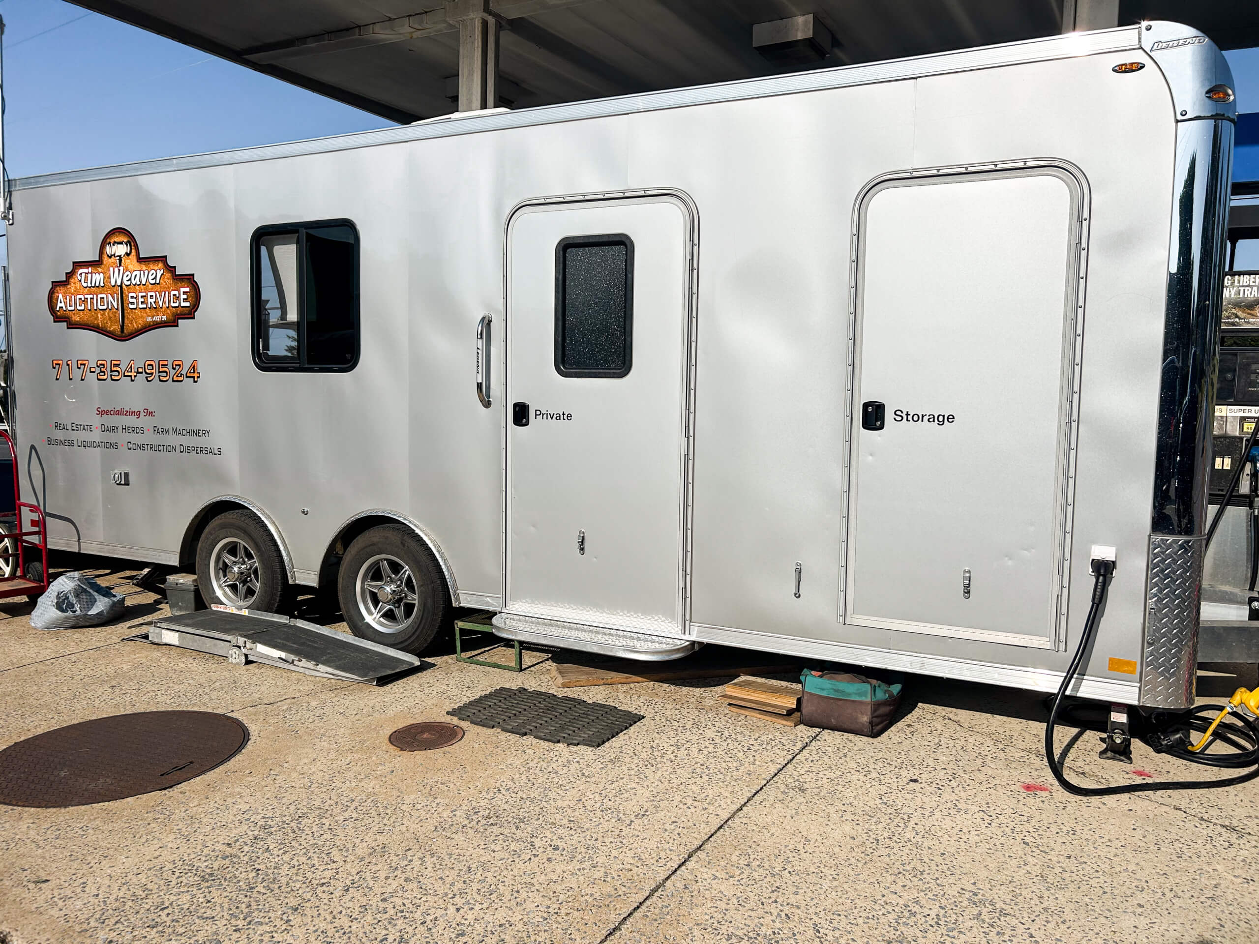 Tim Weaver Auction Service Lancaster County PA A silver trailer parked on a concrete surface, labeled with business signage for an auction service and two doors marked "Private" and "Storage.