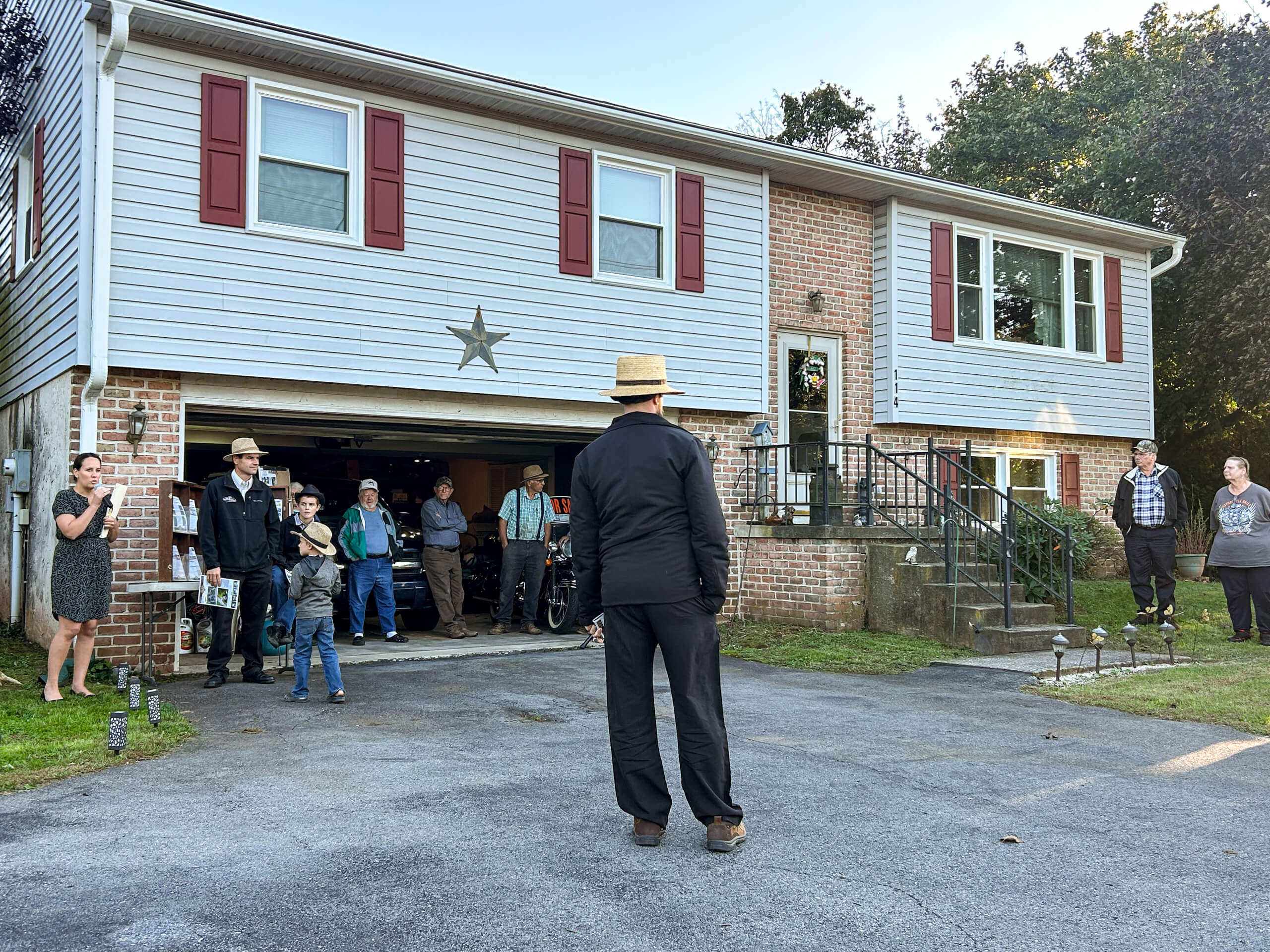 Tim Weaver Auction Service Lancaster County PA A group of people, some in traditional attire, stand outside a two-story house with a star decoration above the garage and open garage door.