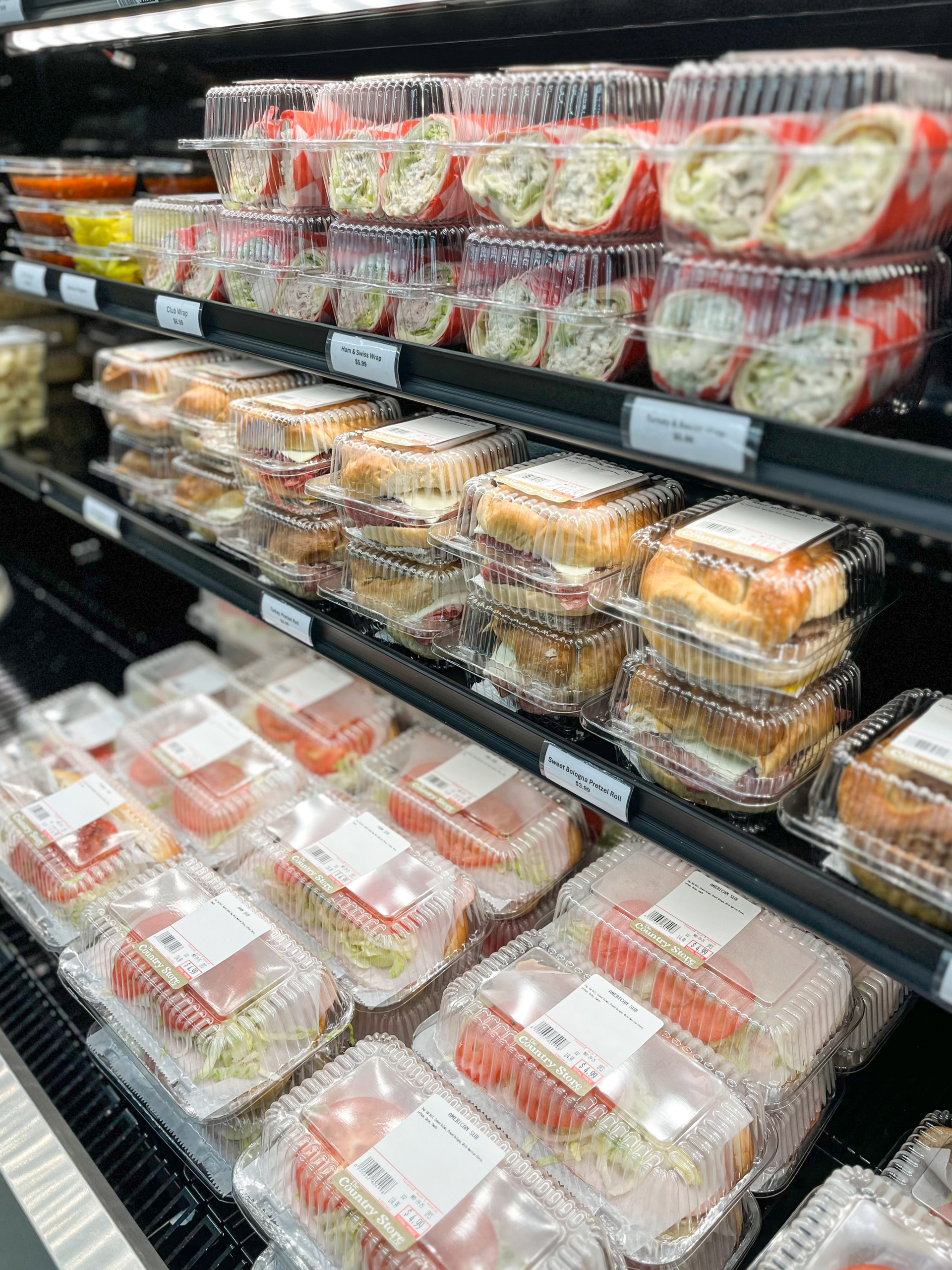 The Country Store Mount Joy PA Plastic containers with pre-made sandwiches and wraps are neatly stacked on shelves in a refrigerated display case at a store or deli.