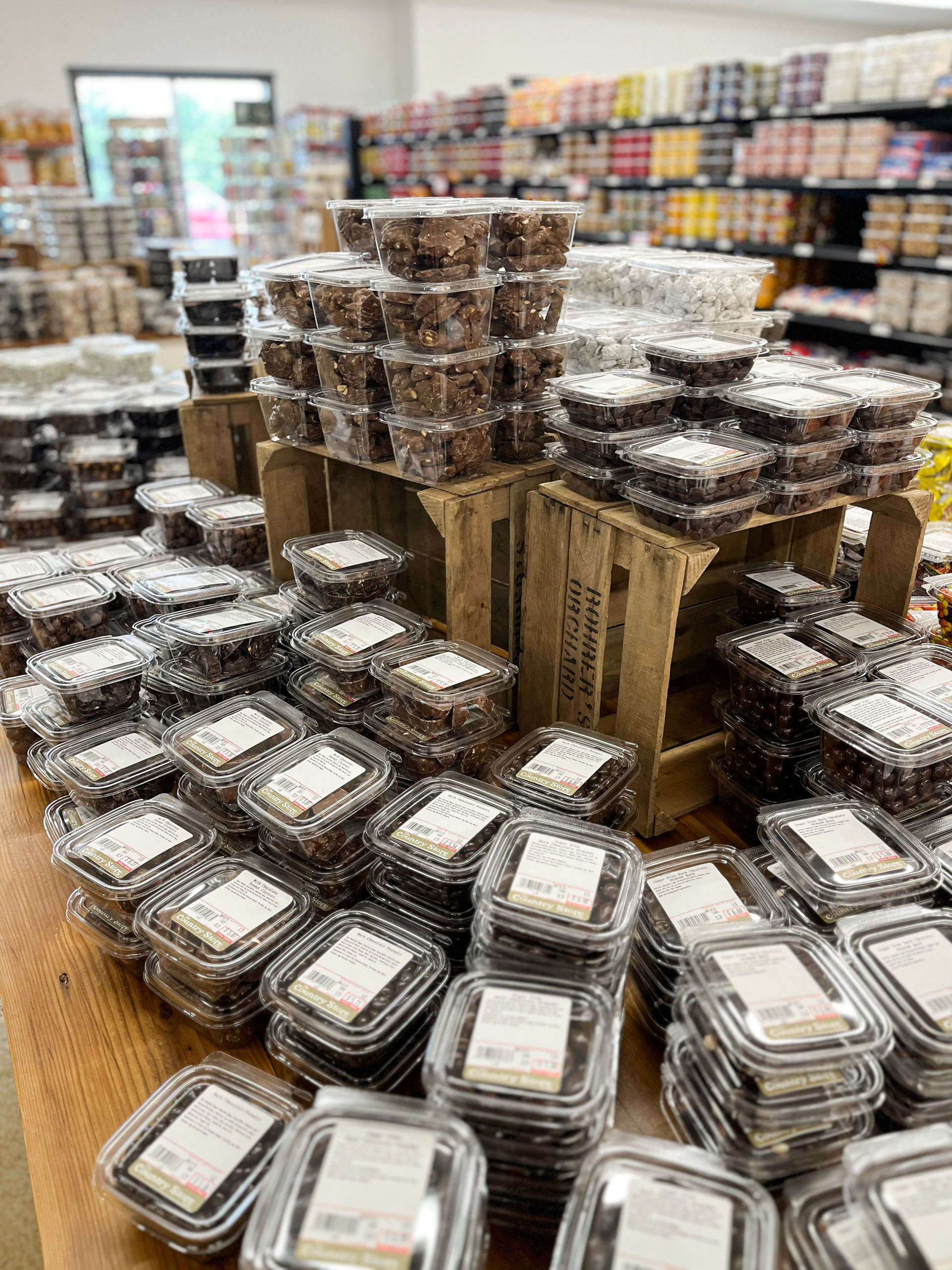 The Country Store Mount Joy PA Plastic containers filled with dates and dried fruits are stacked on a table and wooden crates inside a grocery store. Shelves with assorted products are visible in the background.