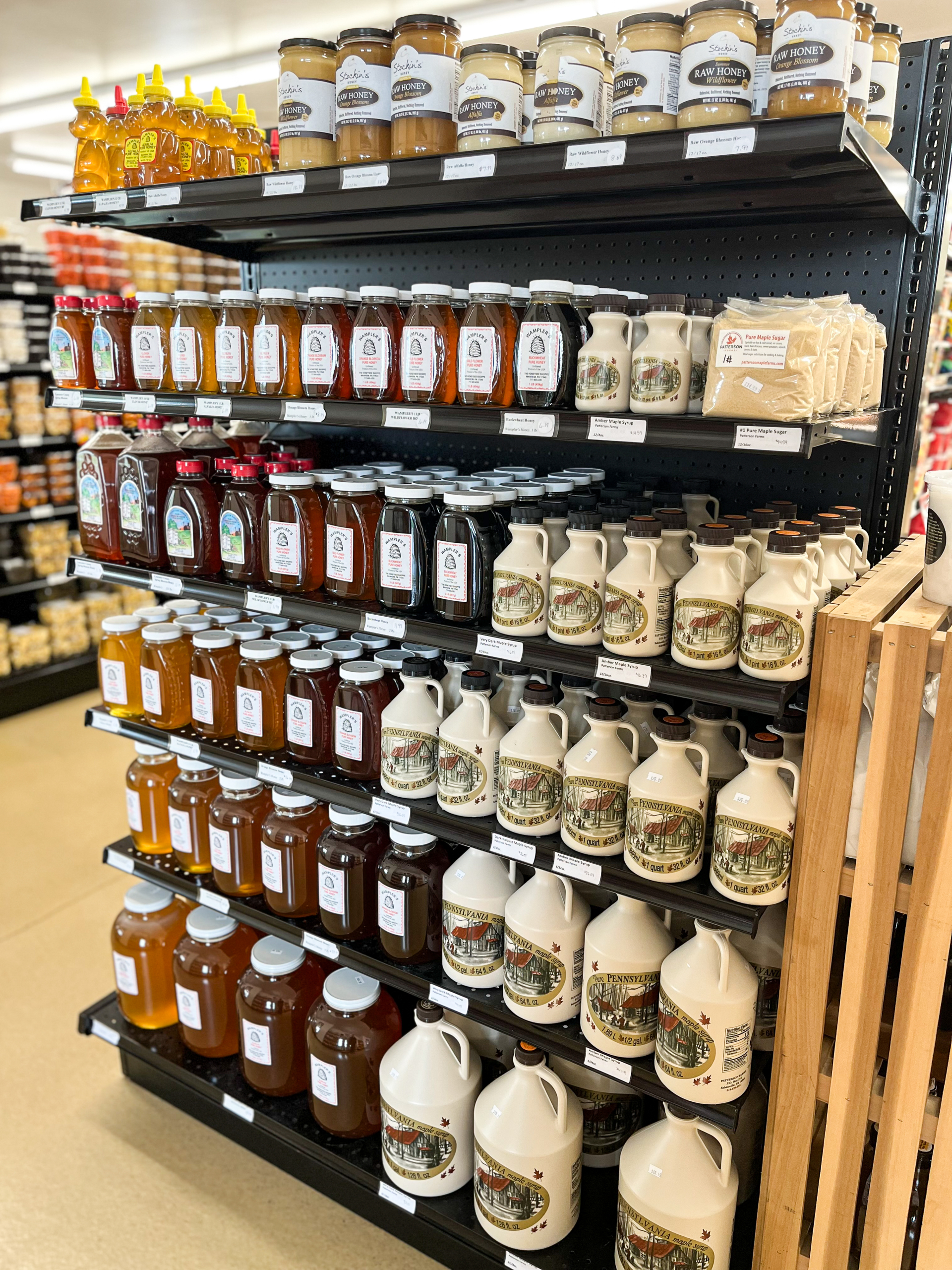 11.24.25 The Country Store Gallery 1-4 Shelves display bottles and jars of honey, maple syrup, and preserves in a store. Different sizes and brands are arranged in neat rows.
