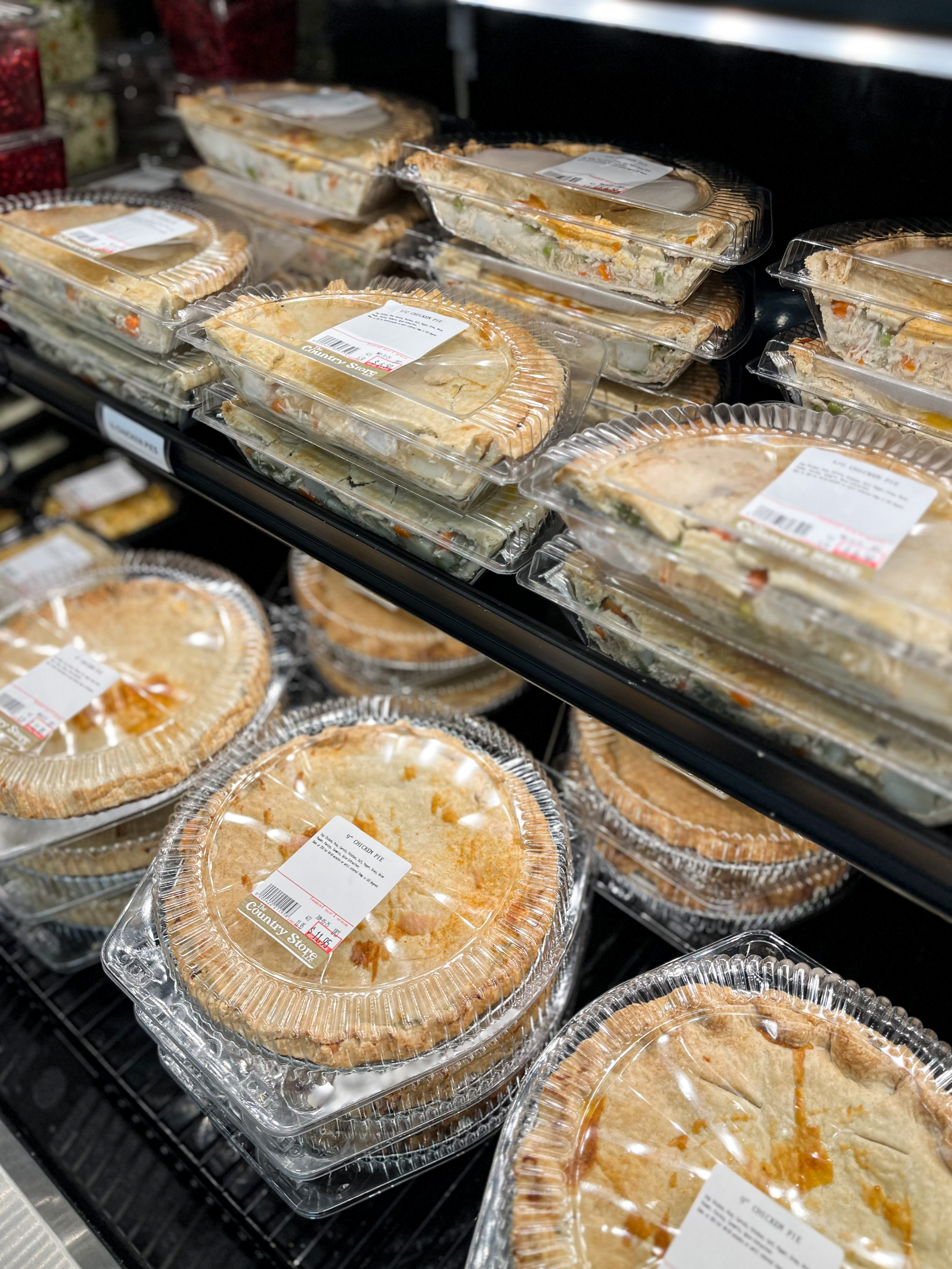 11.24.25 The Country Store Gallery 1-6 Shelves of packaged pot pies in clear plastic containers on display in a grocery store refrigerated section.
