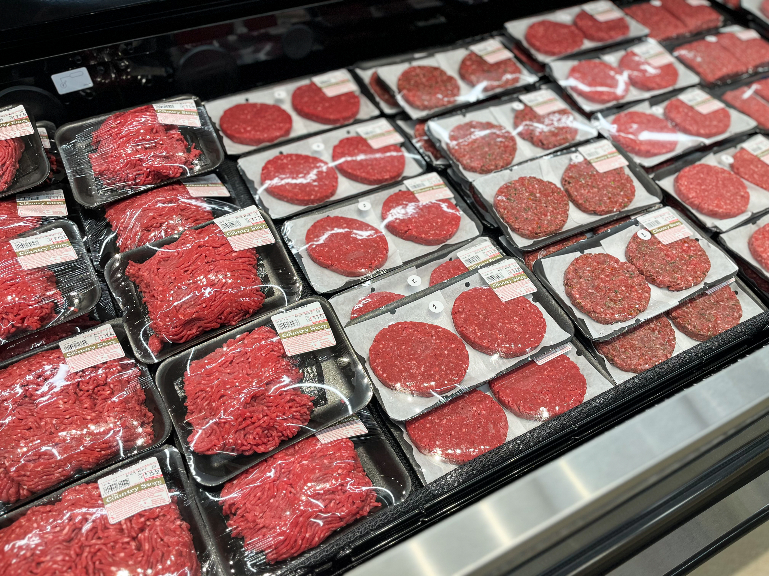 The Country Store Mount Joy PA Packages of ground beef and beef patties arranged on shelves in a grocery store refrigerated meat section.