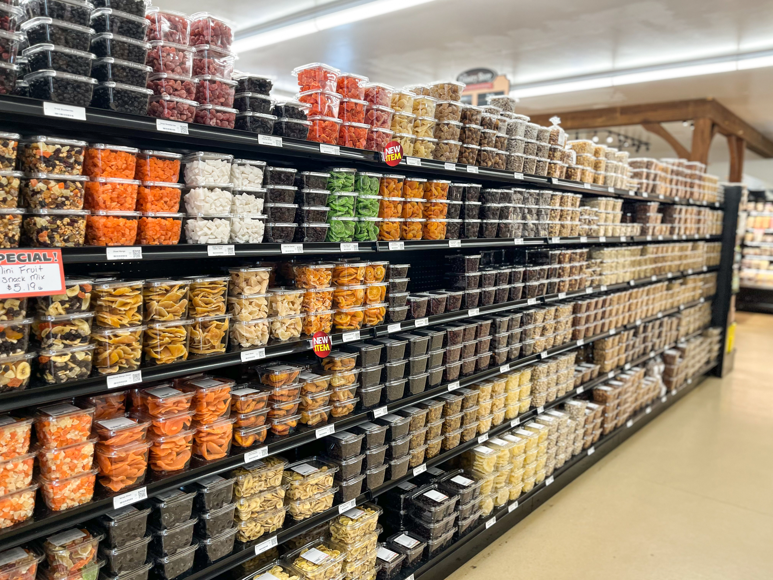 The Country Store Mount Joy PA Shelves in a grocery store filled with clear plastic containers of assorted dried fruits, nuts, and snacks, neatly stacked in rows.