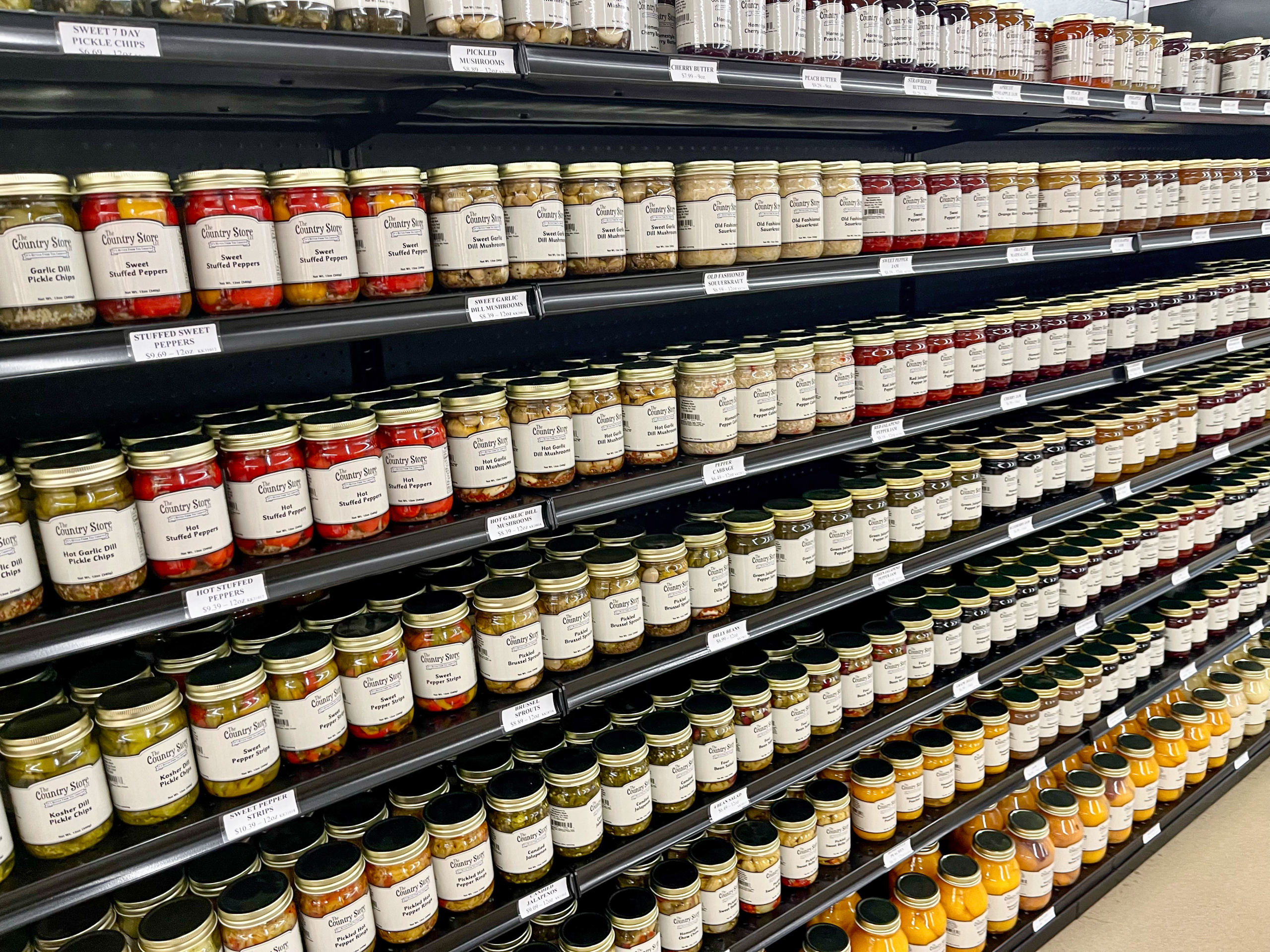 The Country Store Mount Joy PA Shelves stocked with rows of glass jars containing preserved foods such as jams, pickles, and sauces in a grocery store.