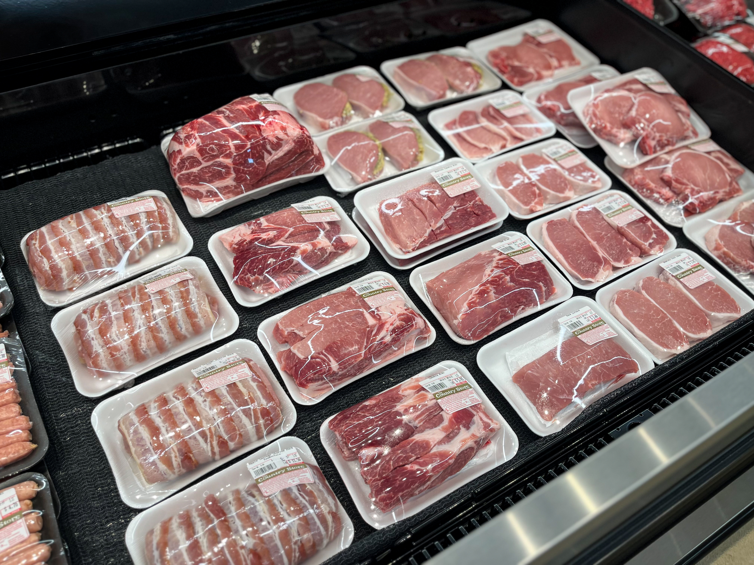 The Country Store Mount Joy PA Various cuts of raw meat, including steaks, chops, and roasts, packaged in plastic trays and displayed in a refrigerated grocery store case.