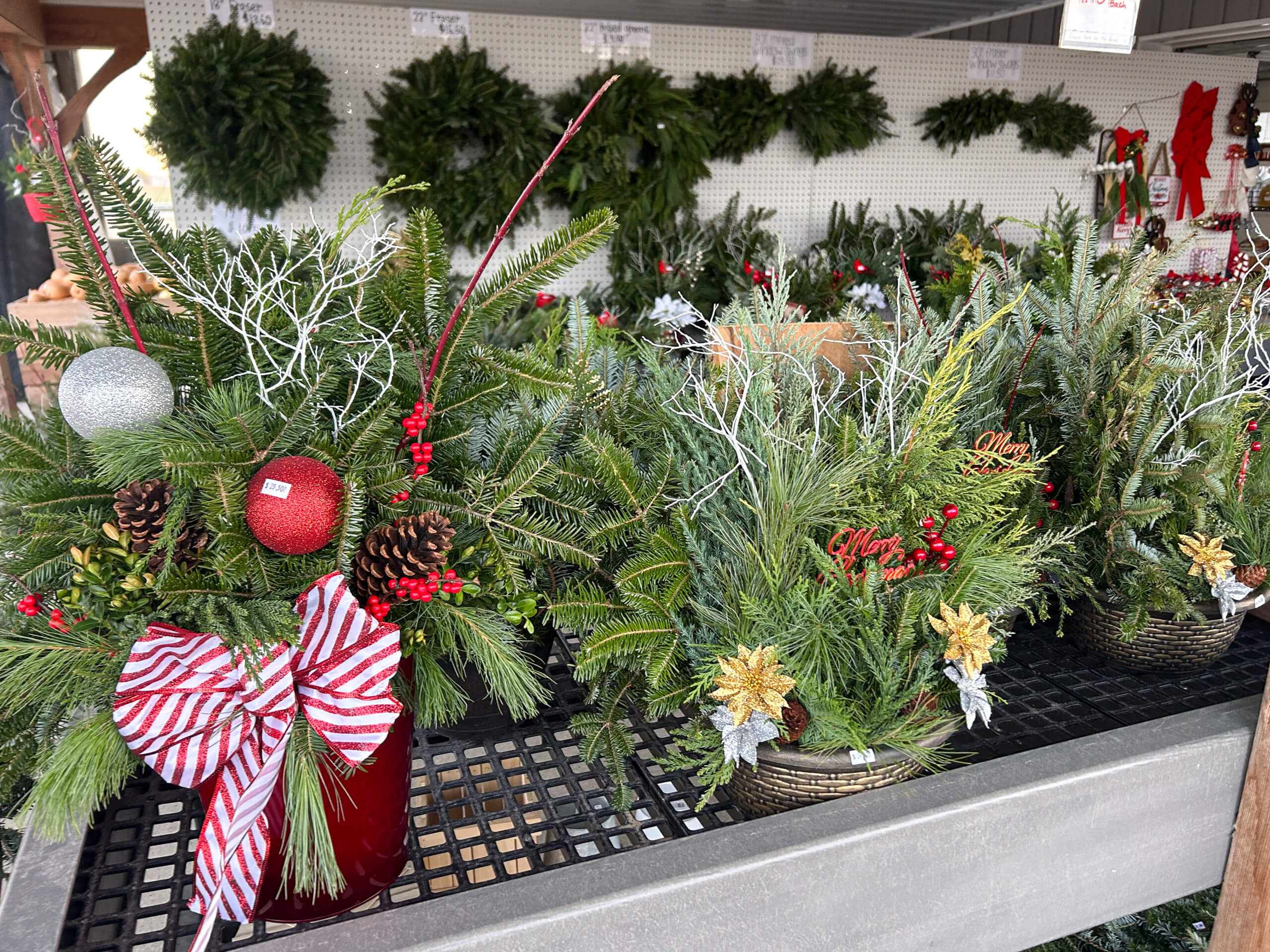 Stoltzfus Produce & Marketfare New Holland PA Christmas wreaths and festive greenery arrangements with ornaments, ribbons, and pinecones displayed on shelves at a market or garden center.