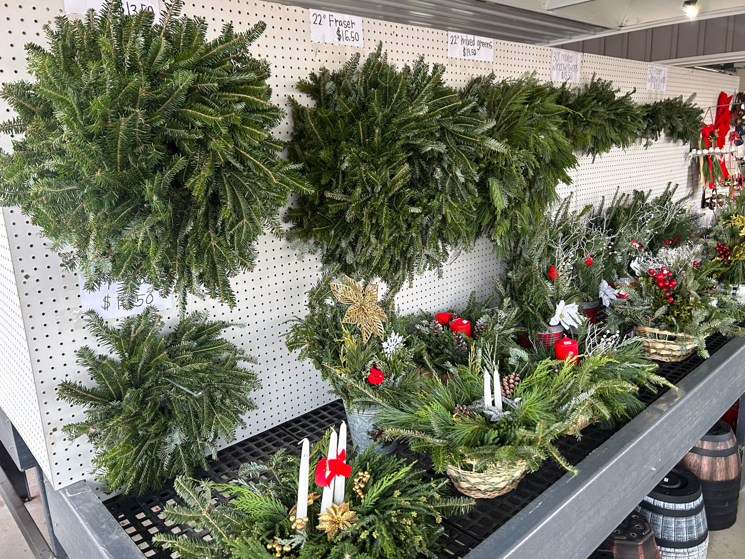 Stoltzfus Produce & Marketfare New Holland PA Various fresh evergreen wreaths and holiday centerpieces with candles and bows are displayed for sale on shelves in a store.