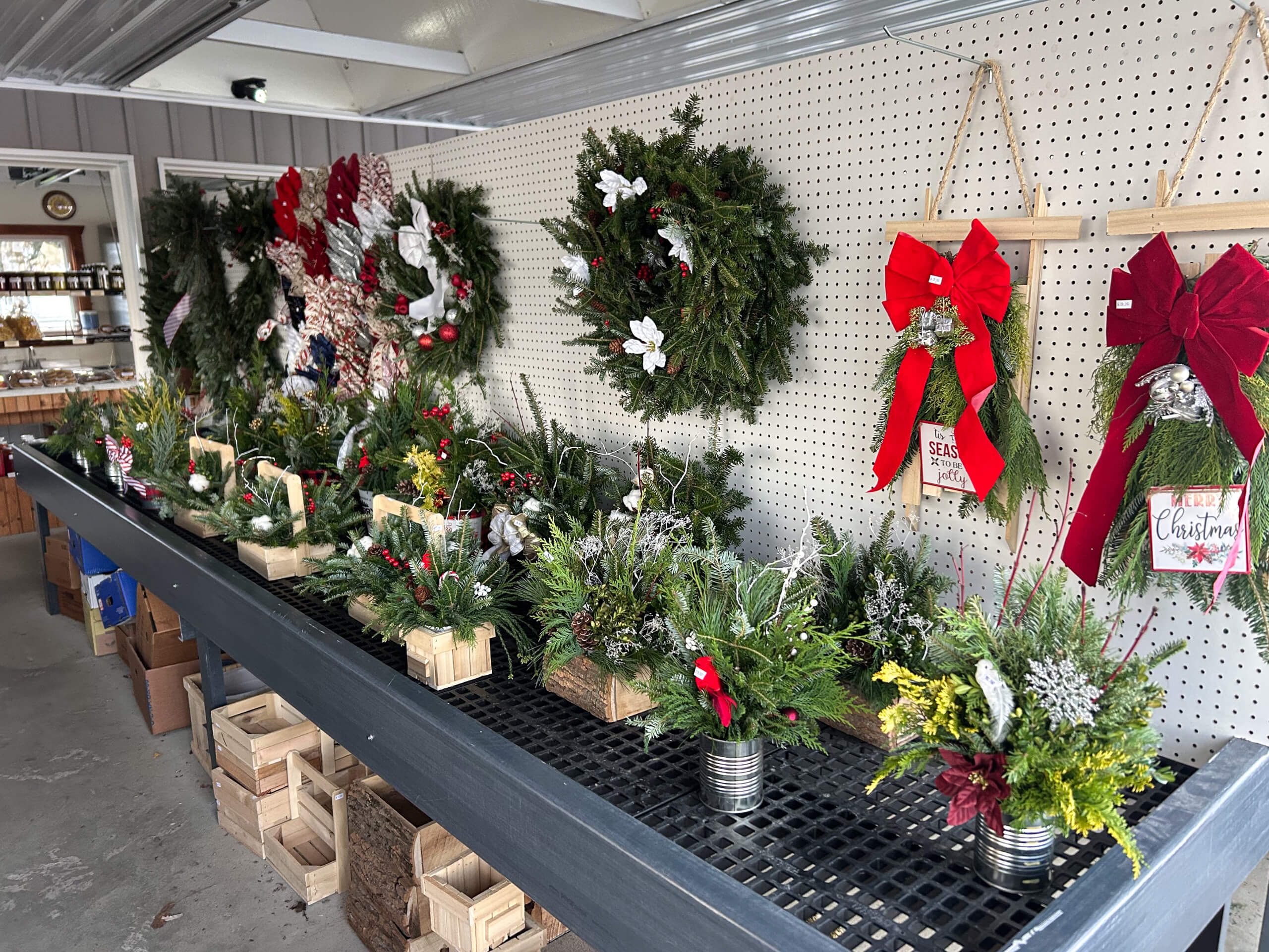 Stoltzfus Produce & Marketfare New Holland PA A display of Christmas wreaths and festive floral arrangements on shelves, featuring greenery, red bows, and holiday decorations inside a shop.
