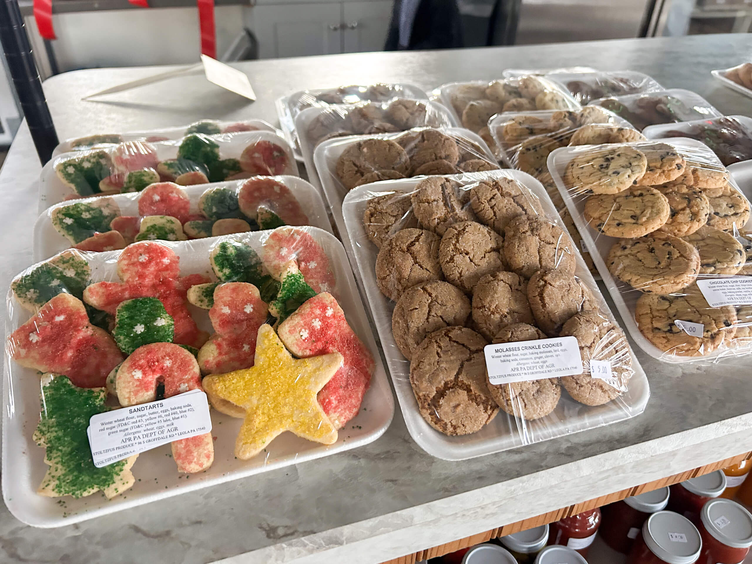 Stoltzfus Produce & Marketfare New Holland PA Assorted holiday-themed cookies and packaged cookies, including sugar cookies with festive sprinkles and chocolate chip cookies, displayed on a marble countertop.