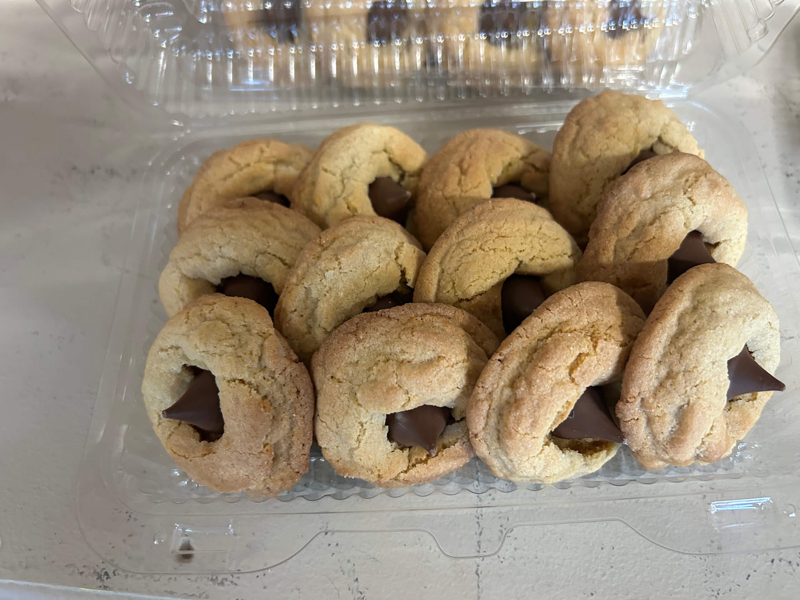 Turtle Hill Farm Market Leola PA Plastic container filled with peanut butter blossom cookies, each topped with a Hershey's Kiss chocolate, on a light-colored surface.