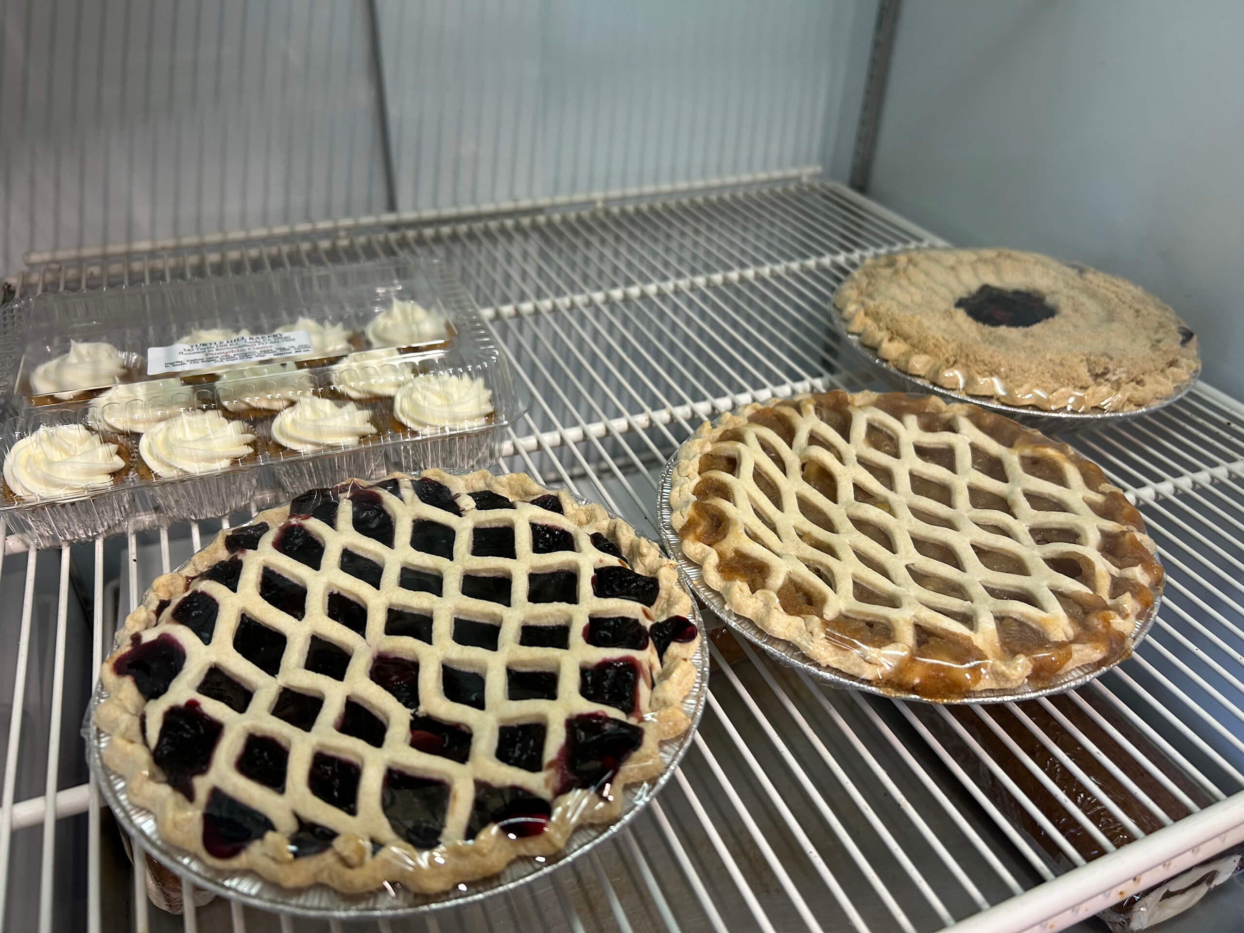 Turtle Hill Farm Market Leola PA Three lattice-topped pies and a container of cupcakes are displayed on mostly empty refrigerator shelves.