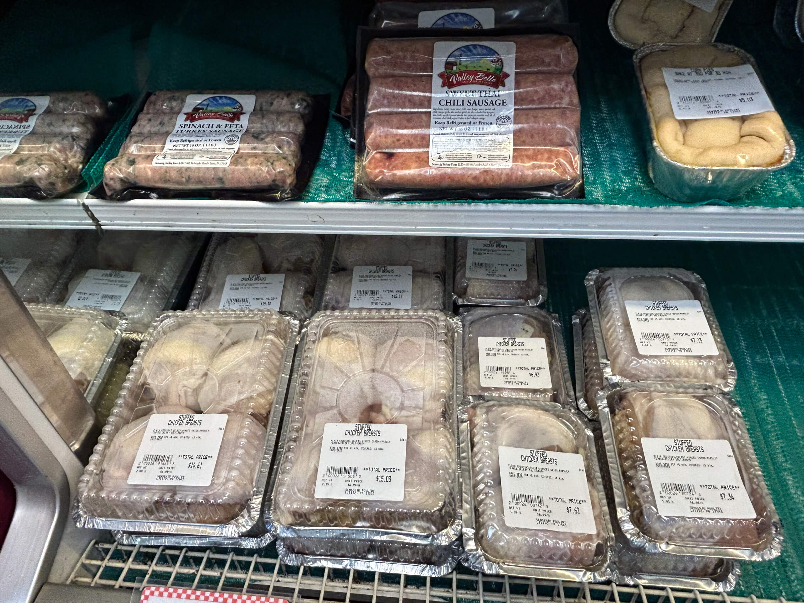 Sensenig Poultry Lititz PA Packaged sausages and trays of frozen baked goods are displayed on metal shelves inside a refrigerated section at a store.