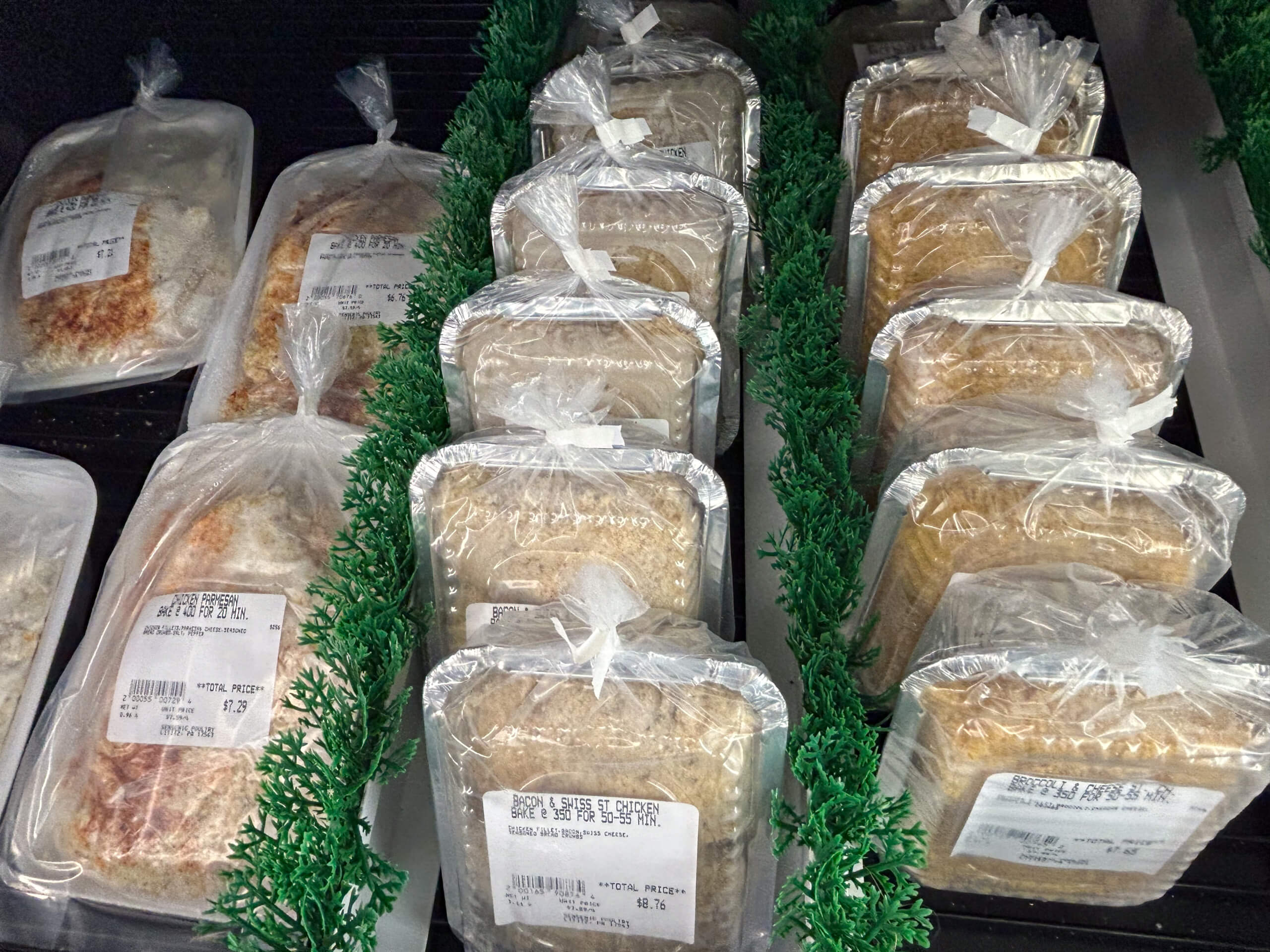 Sensenig Poultry Lititz PA Packages of food wrapped in clear plastic and labeled with price stickers are arranged in rows on a grocery store shelf with green decorative dividers.