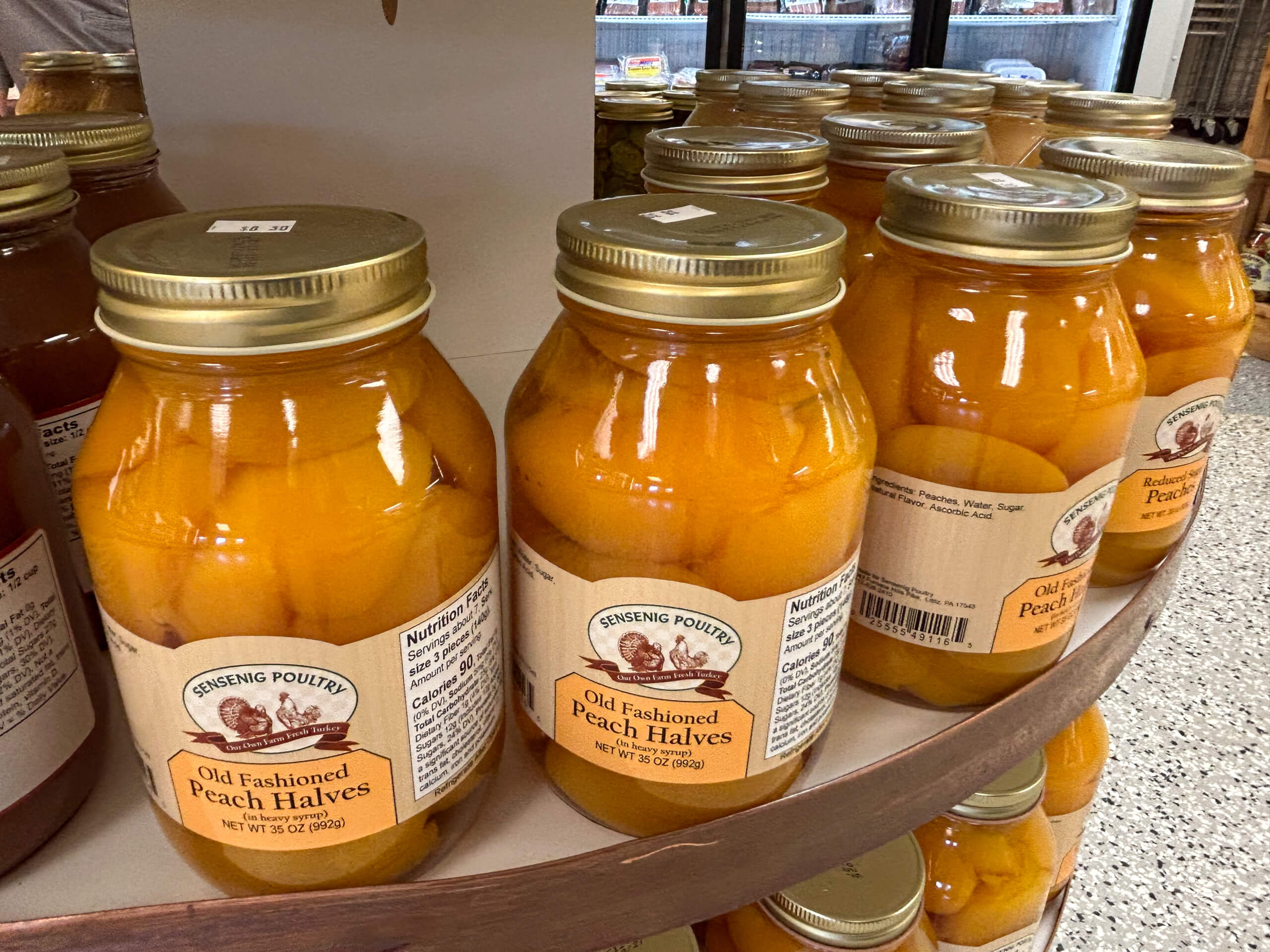Sensenig Poultry Lititz PA Several jars of Old Fashioned Peach Halves in syrup are displayed on a curved shelf in a grocery store.