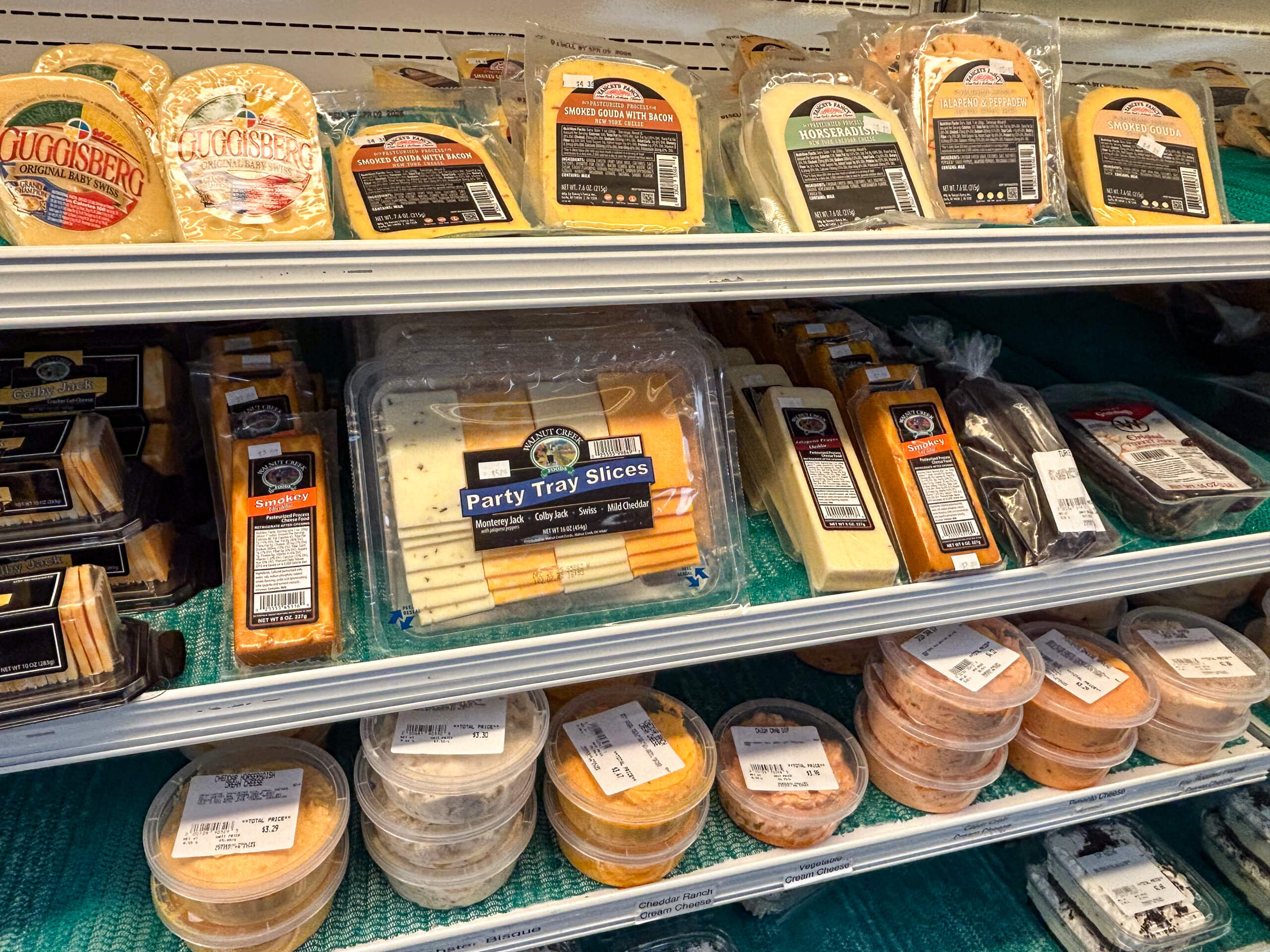 Sensenig Poultry Lititz PA Shelves stocked with various packaged cheeses, cheese slices, and cheese spreads in a refrigerated grocery display.