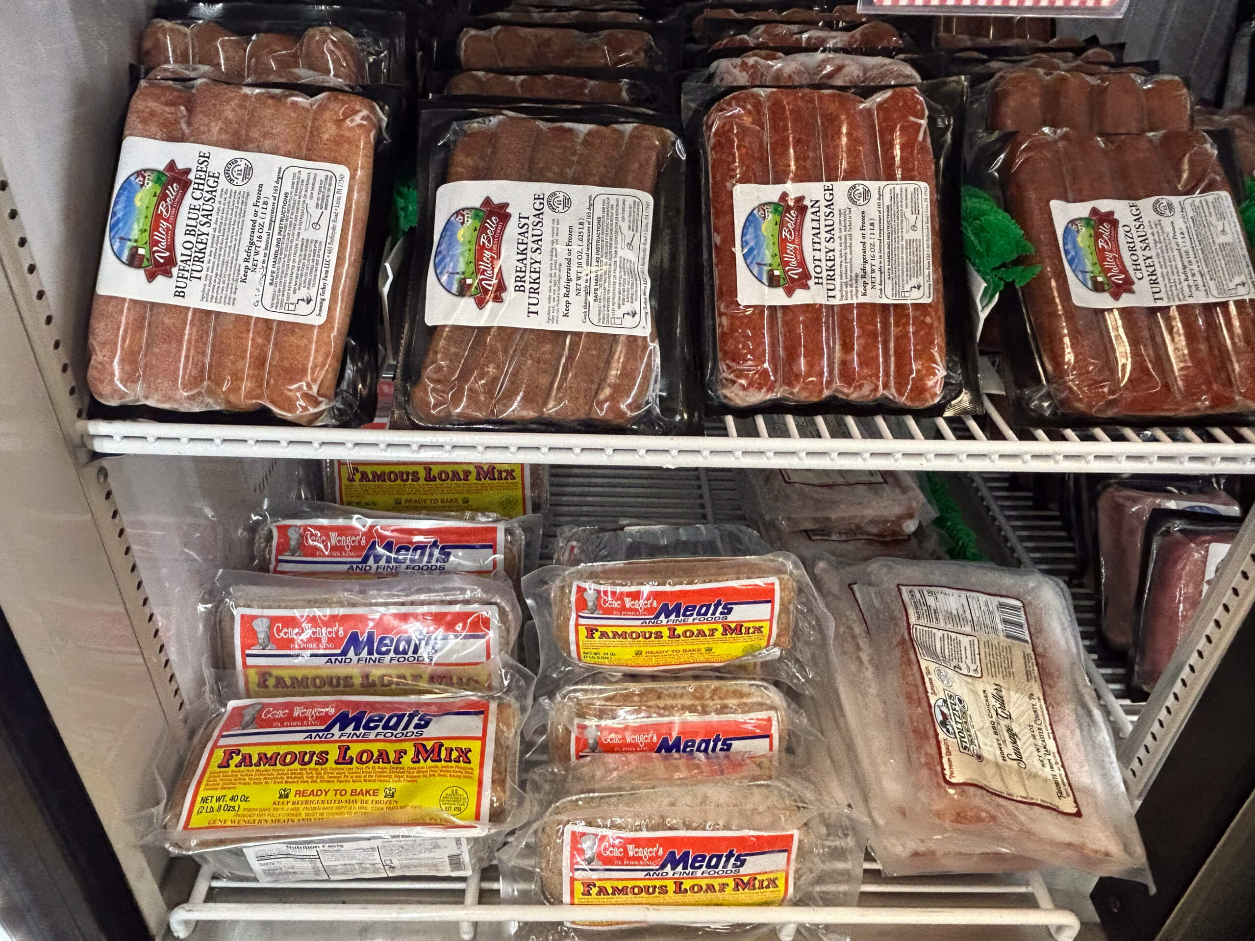 Sensenig Poultry Lititz PA Packages of turkey sausage and loaf mix are stacked on shelves inside a refrigerated display case at a store.