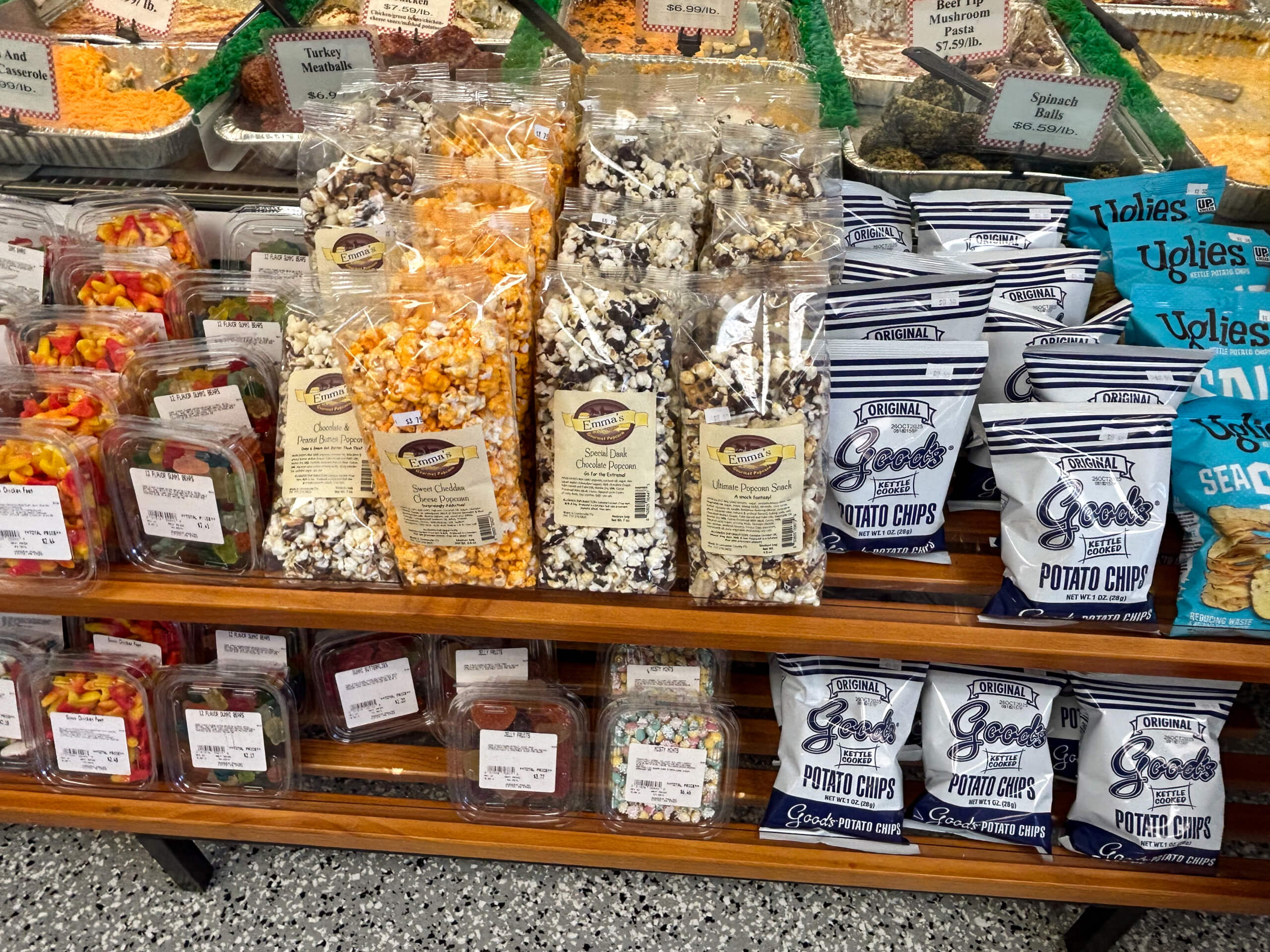 Sensenig Poultry Lititz PA Bags of popcorn and potato chips are displayed on shelves alongside containers of fruit and baked goods in a grocery store.