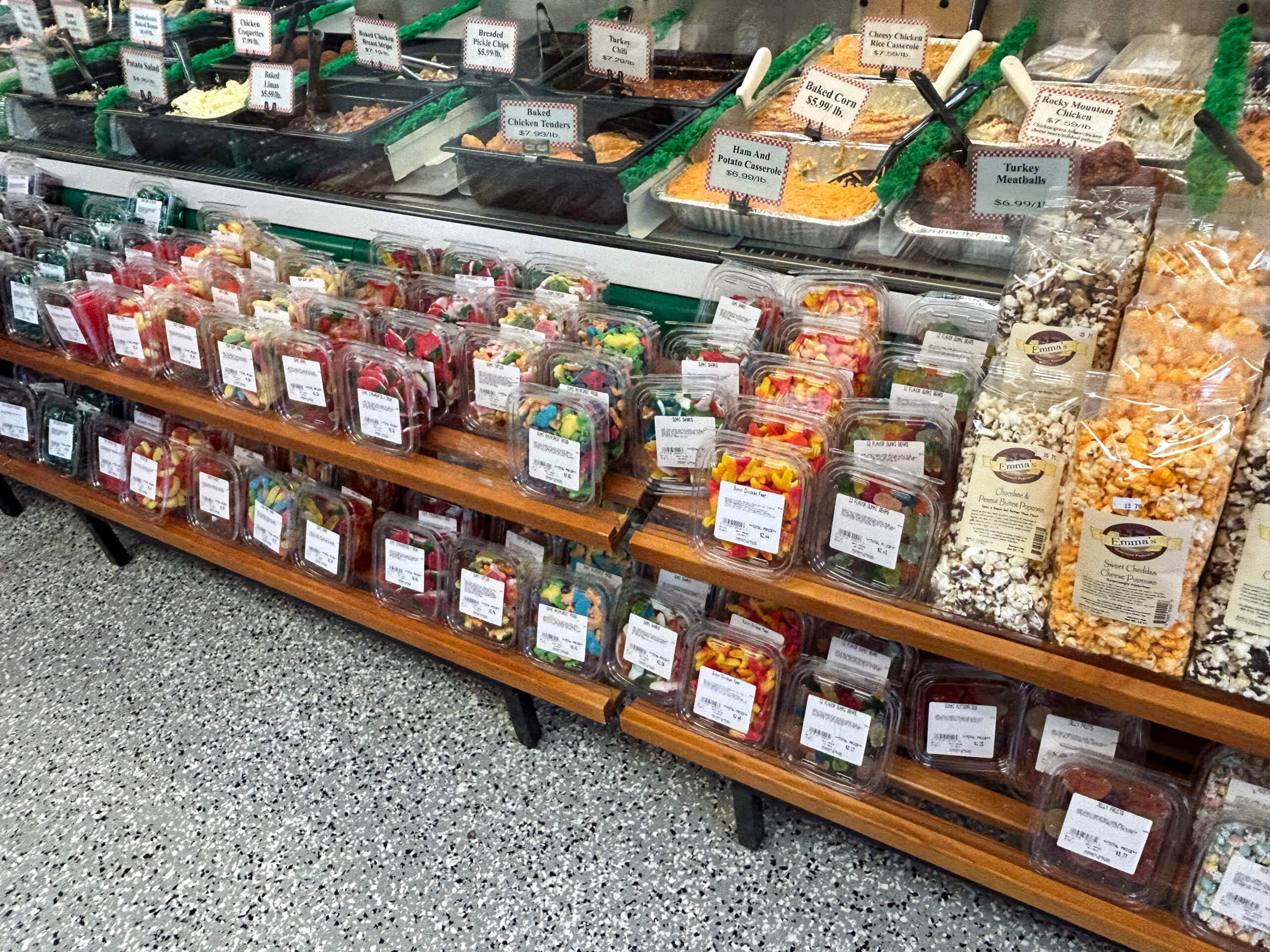 Sensenig Poultry Lititz PA Shelves display assorted packaged candies and snacks in clear plastic containers, with bins of bulk treats and popcorn varieties above the shelves in a store setting.