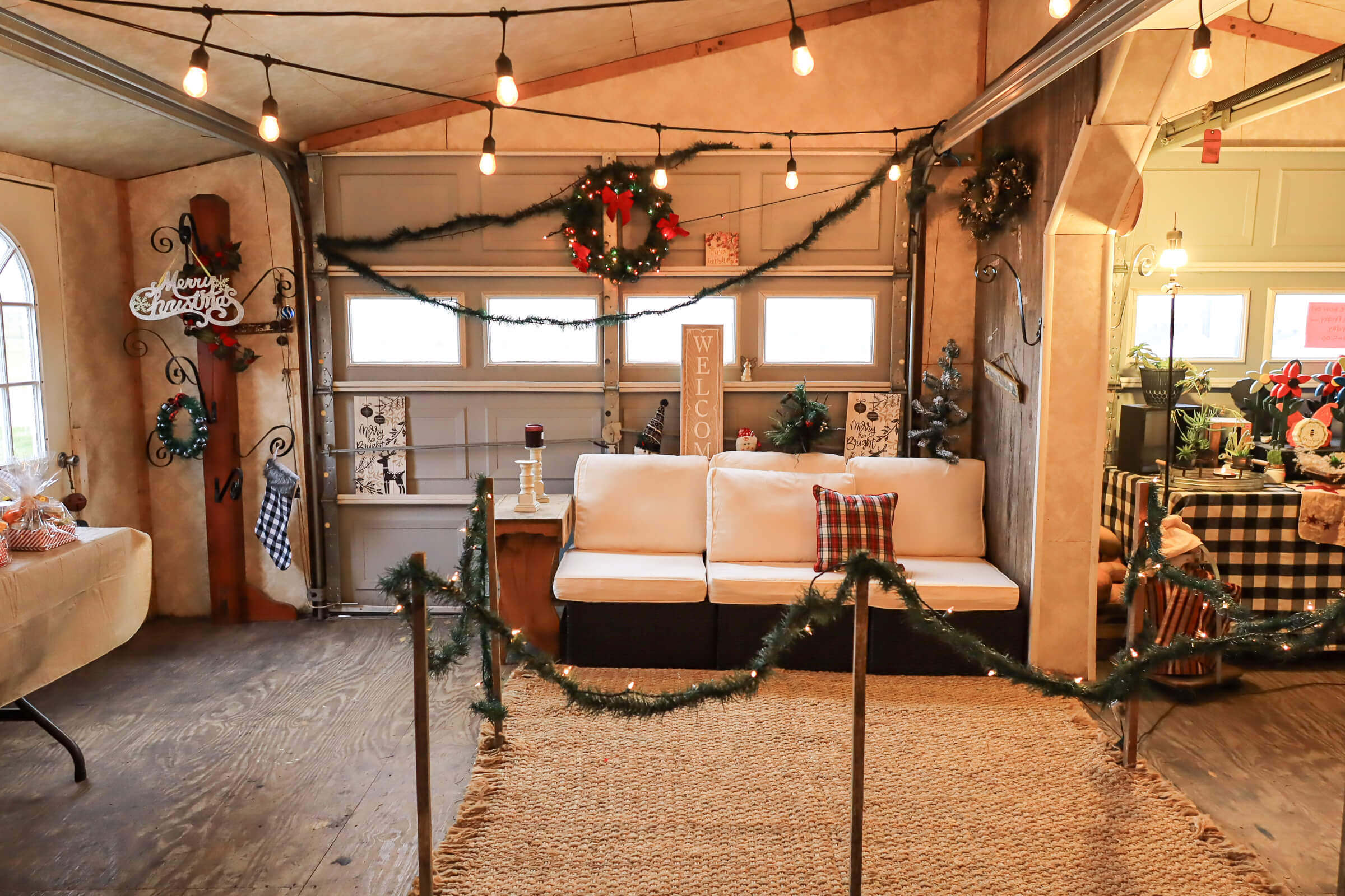Busy Bee's Farm Market Ronks PA A cozy room with a white couch, holiday decorations, garlands, and string lights. The area is roped off with greenery, and festive wreaths hang on the walls and above windows.