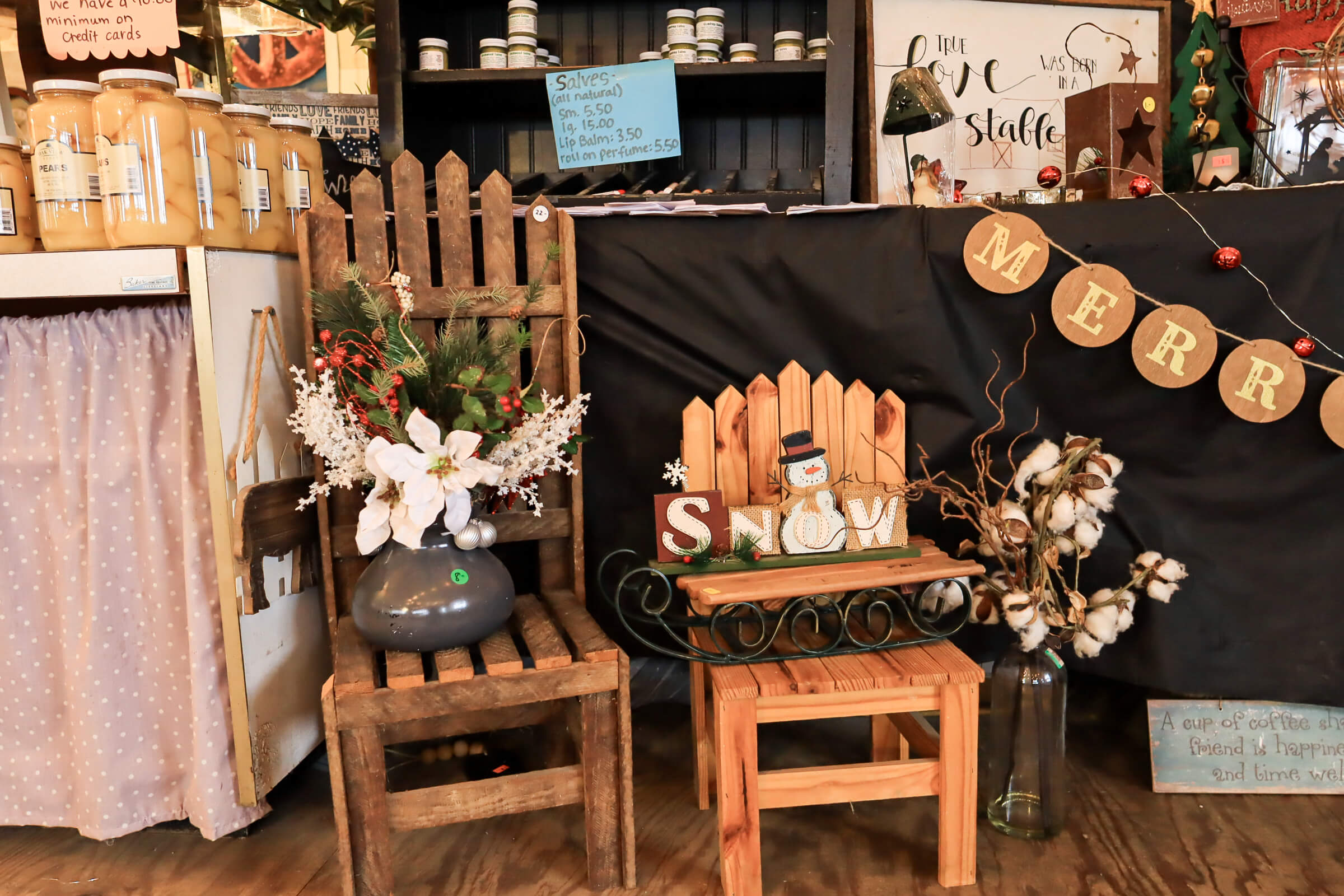 Busy Bee's Farm Market Ronks PA A rustic indoor display features a small wooden chair with a "SNOW" sign, artificial flowers, and holiday decorations including a "MERRY" banner and a snowman figurine.