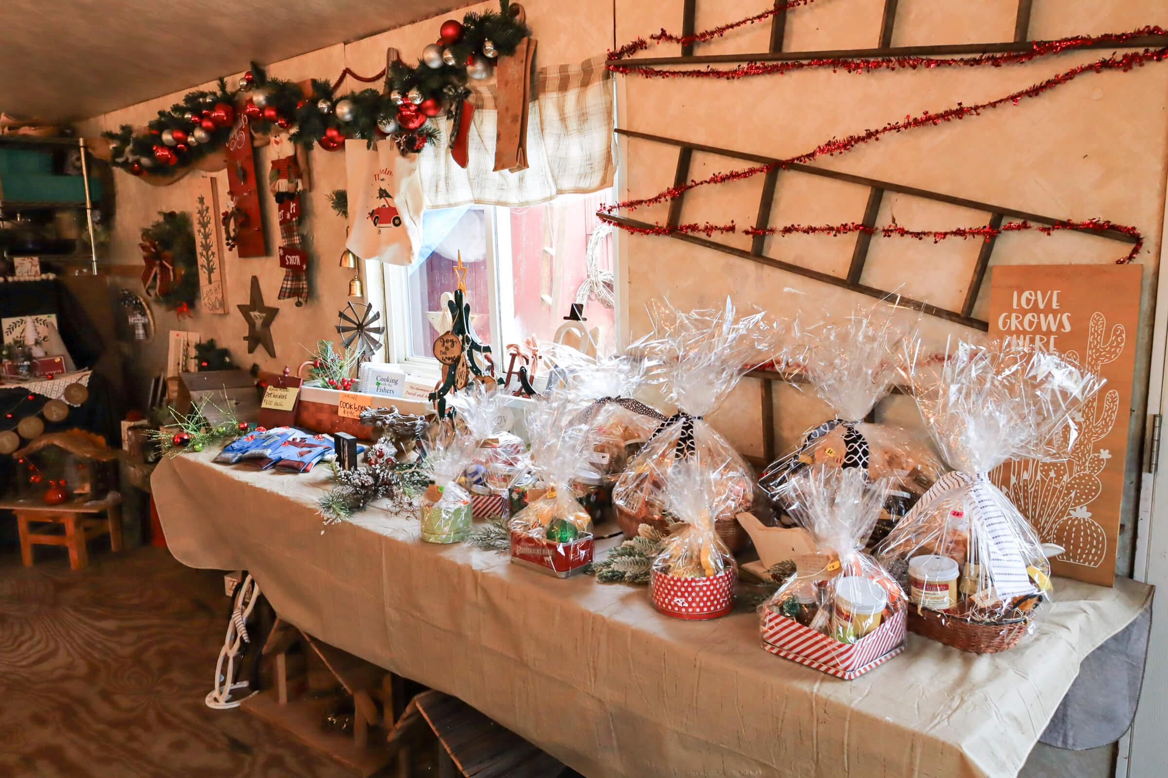 Busy Bee's Farm Market Ronks PA A table covered with assorted gift baskets wrapped in cellophane, surrounded by holiday decorations and festive garlands inside a cozy room.