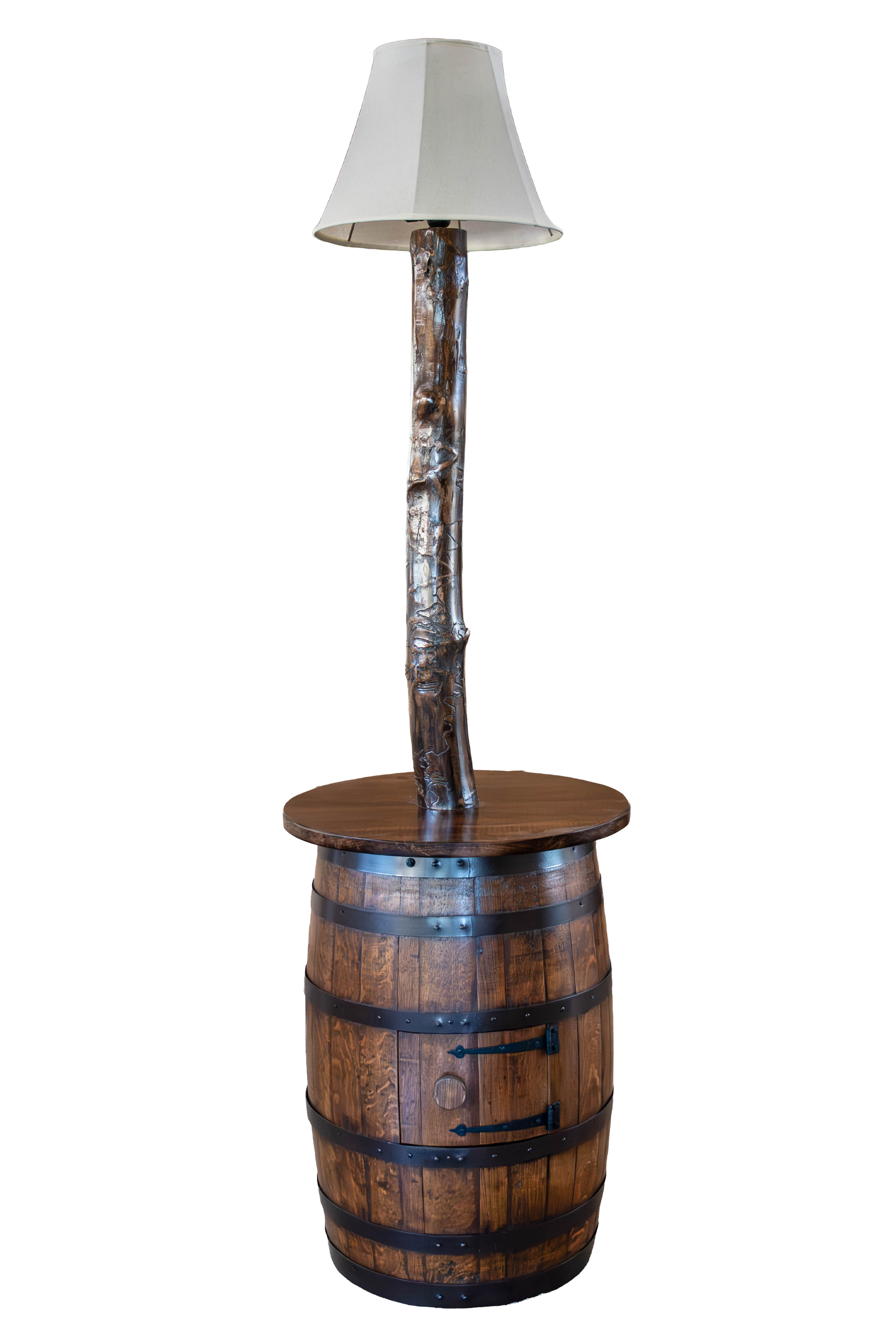 7.8.26 Spring Valley Woodworking Light Fixtures Gallery 1 A rustic lamp with a beige shade is mounted on a wooden post that rises from the center of a round barrel table with metal bands.