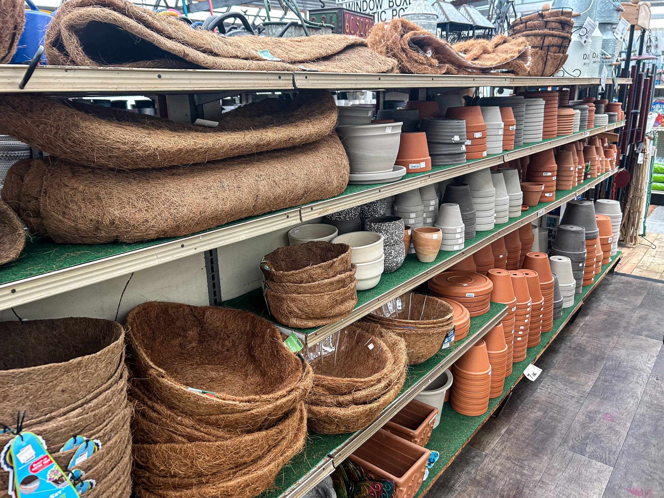 Willow Brook Greenhouse Honey Brook, PA Shelves in a store are stocked with various empty plant pots, planters, and hanging baskets made of clay, plastic, and natural fibers.