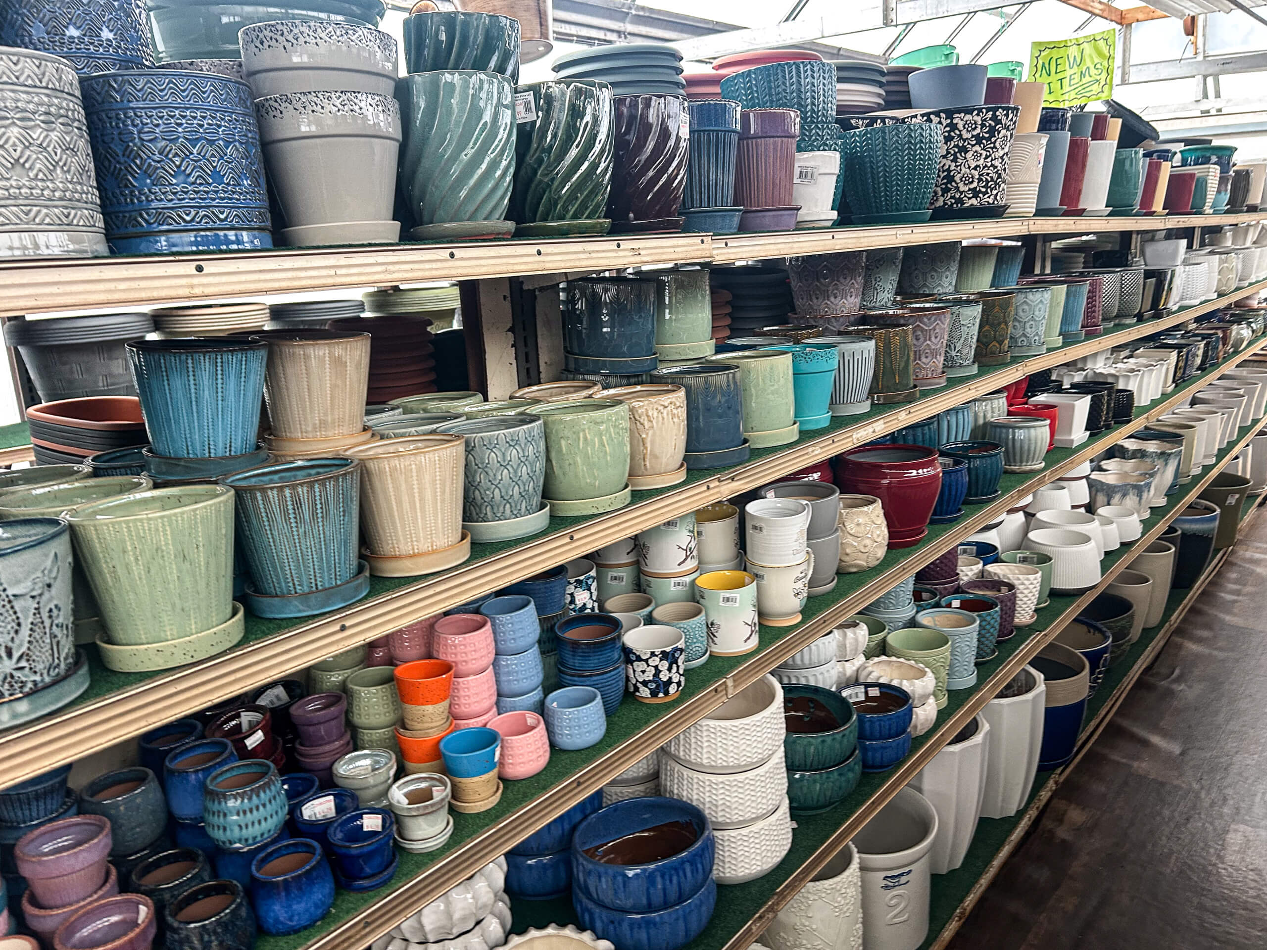 Willow Brook Greenhouse Honey Brook, PA Shelves filled with a variety of colorful ceramic and clay pots in different shapes and sizes displayed in a garden center or store.